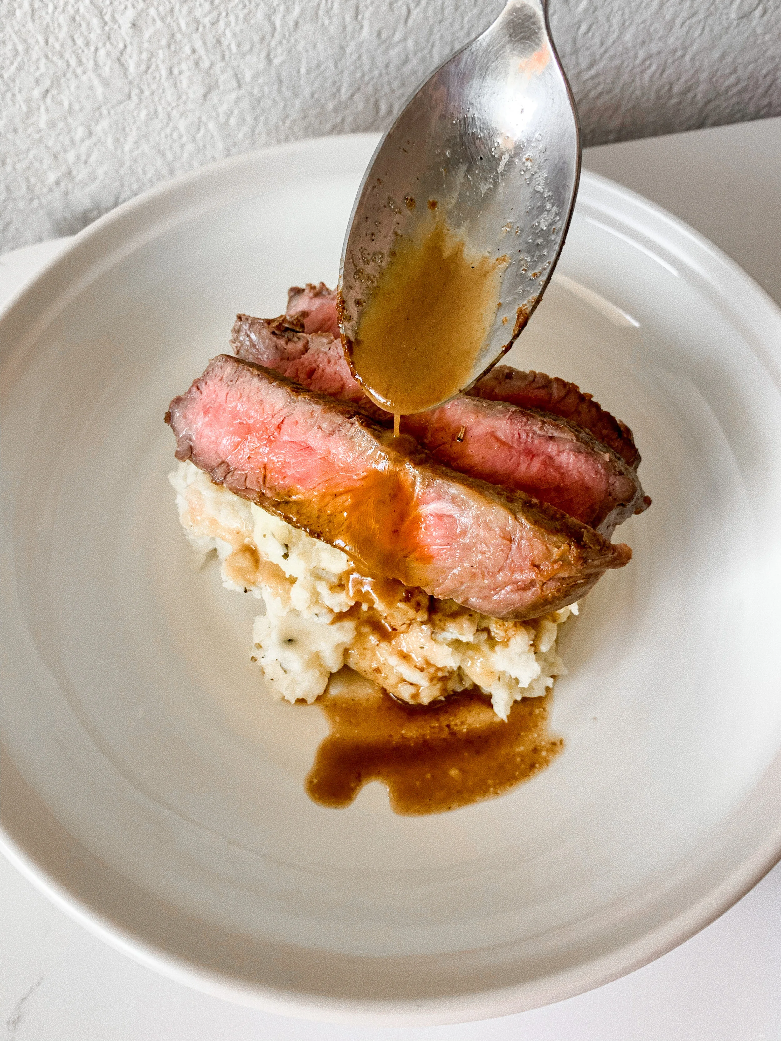 Drizzling the pan sauce over the finished steak and mashed potatoes