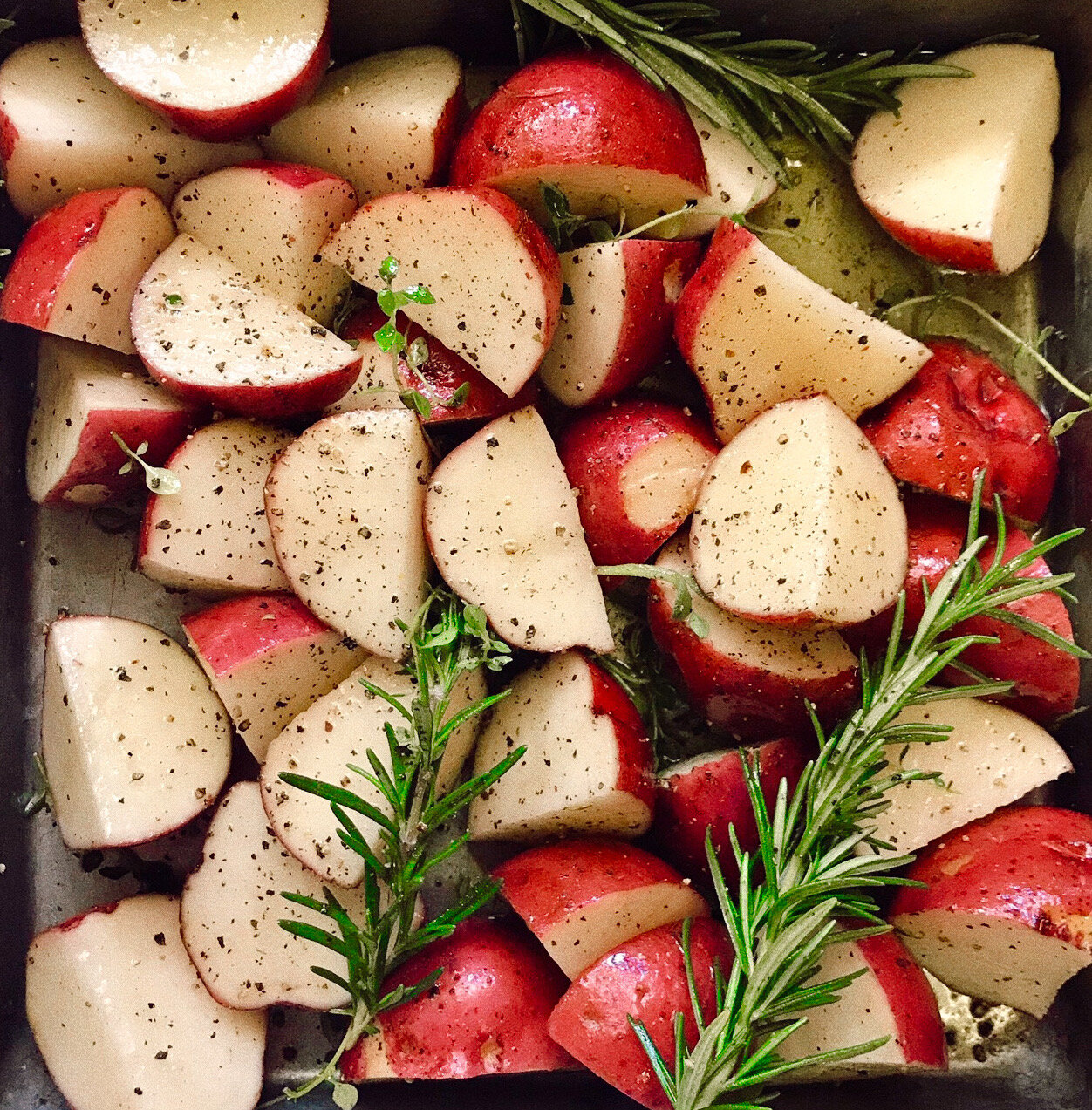Red potatoes mixed with fresh herbs and seasoning ready for the oven