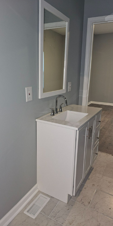 A white bathroom vanity with a built-in sink, silver handles, and a mirror above it, set against a gray wall in a bathroom or laundry area.