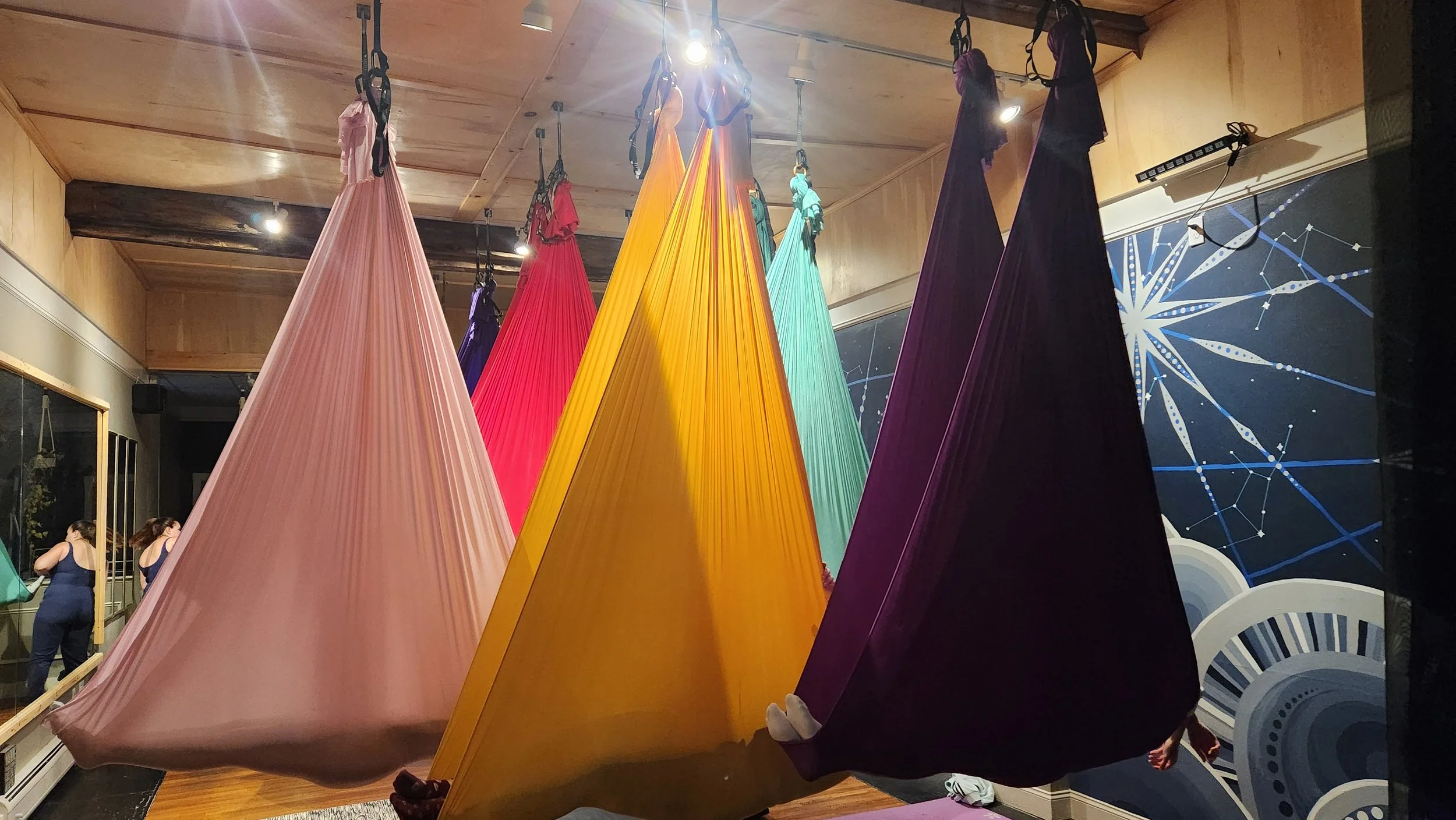 Colorful fabric hammocks hanging from the ceiling in a room with wooden walls and a starry night mural.
