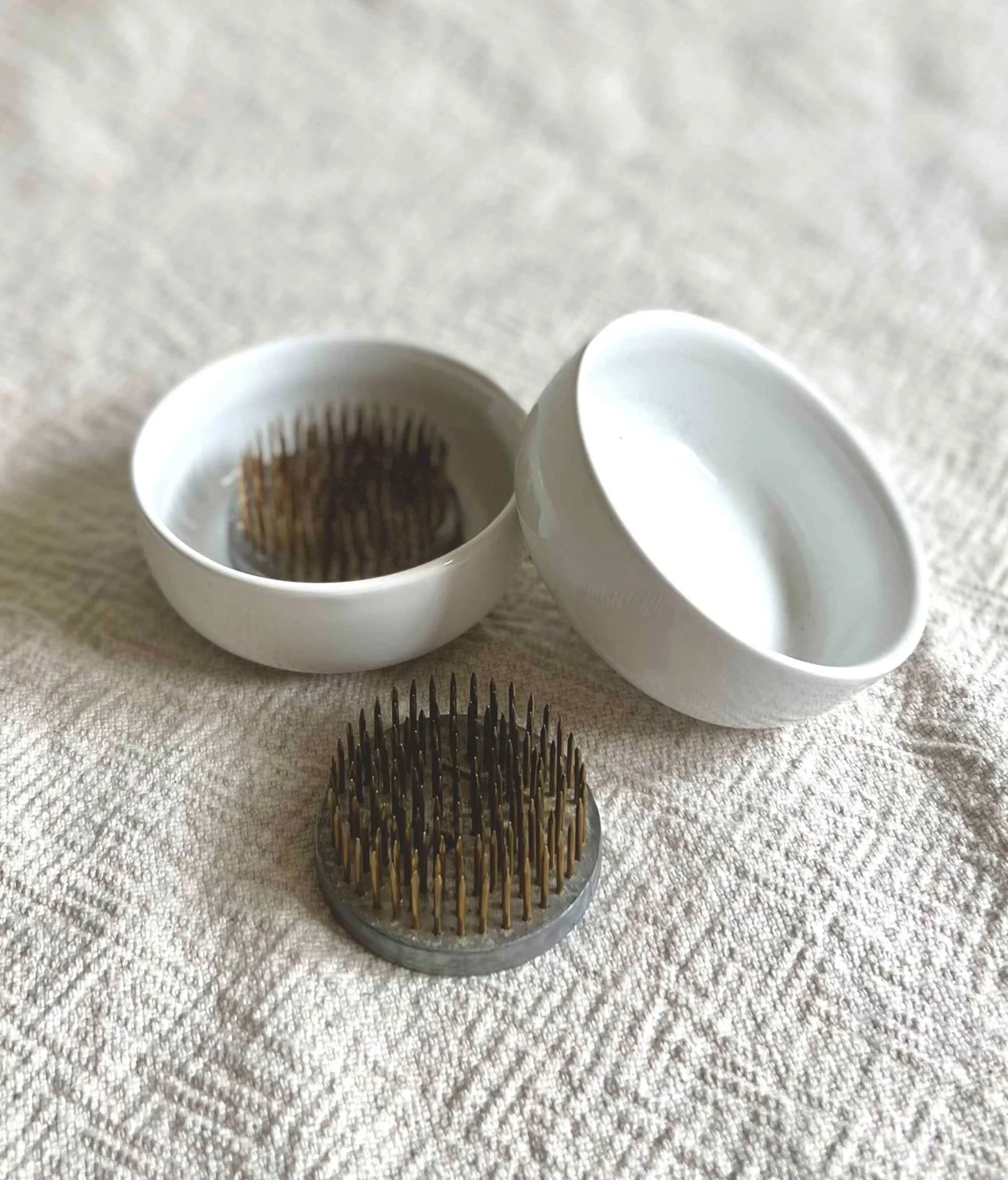 Two white ceramic pin frog cups with two floral pin frogs.