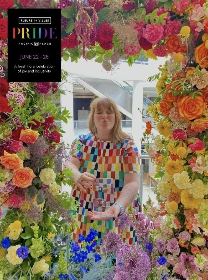 Camile lead designer of New Leaf Floral Design holds the "Best in Show" Award posing in the rainbow Pride installation they made for Fleurs de Villes in June 2023