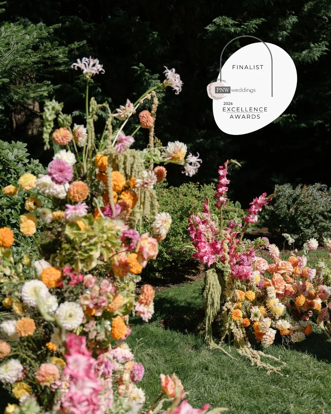 A floral arch at a ceremony in August of 2025 in a color palette of pinks, oranges, peach, green and white.