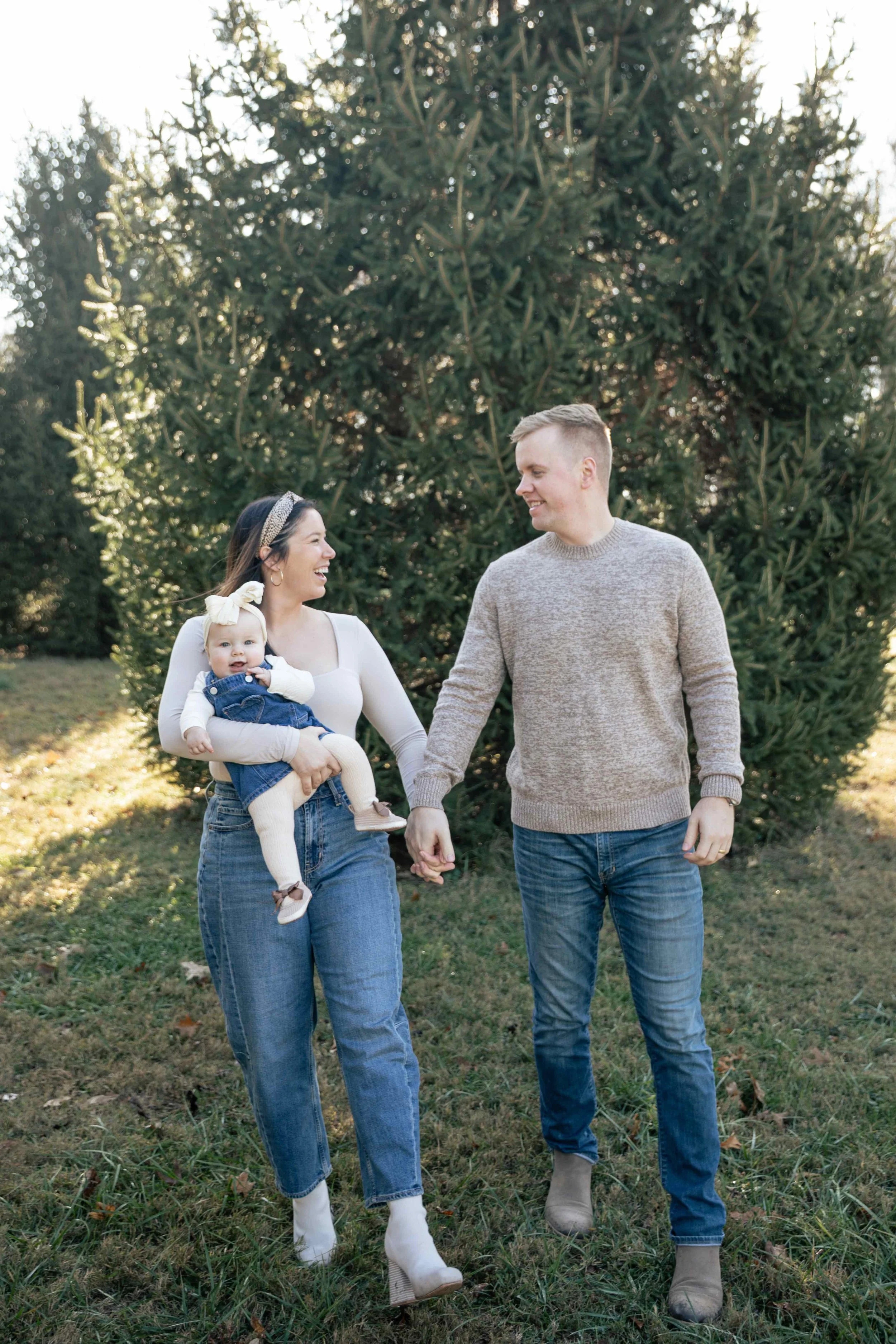 mother and father holding hands walk laughing with baby