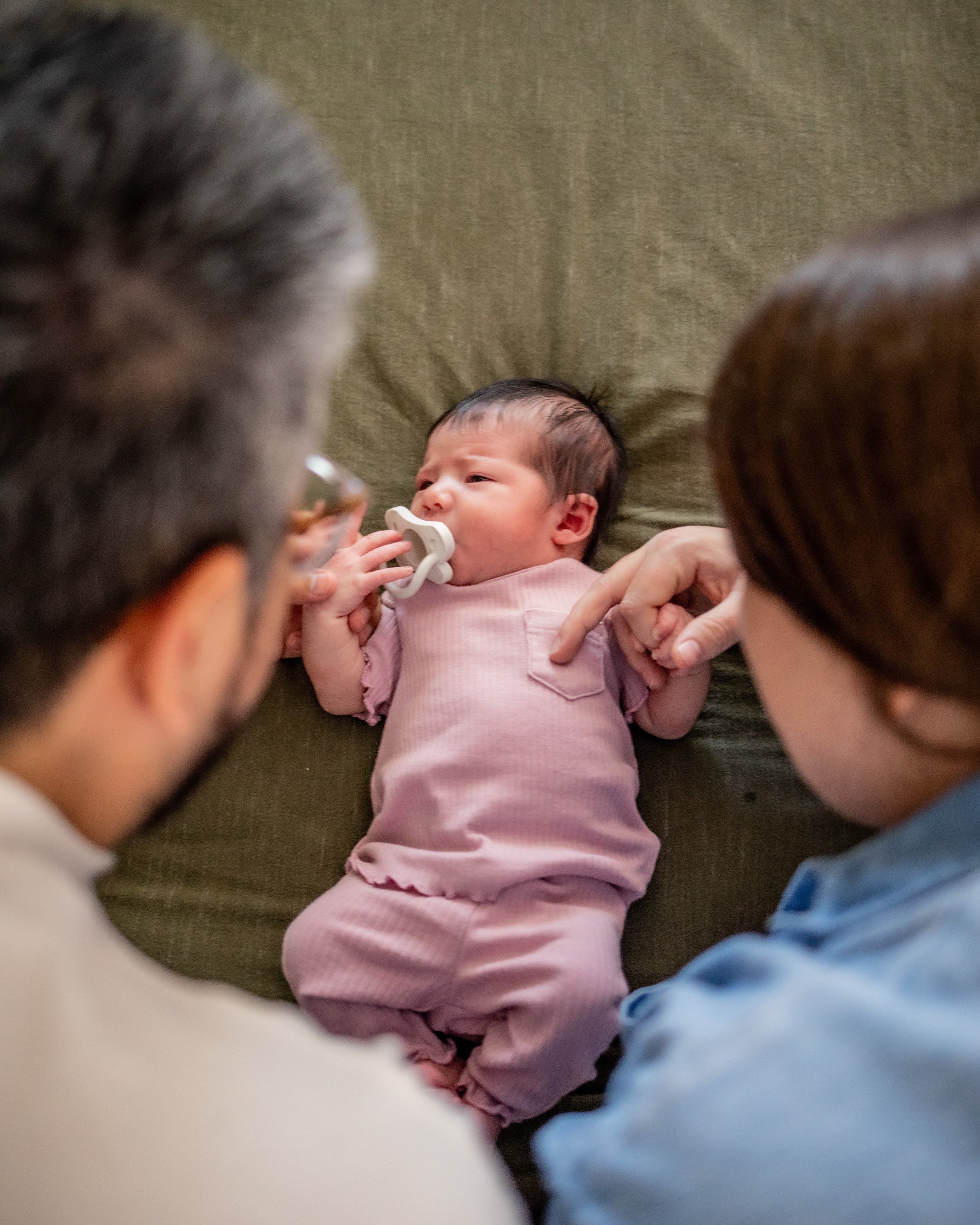 mother and fathering looking at new born baby wearing a pink onesie