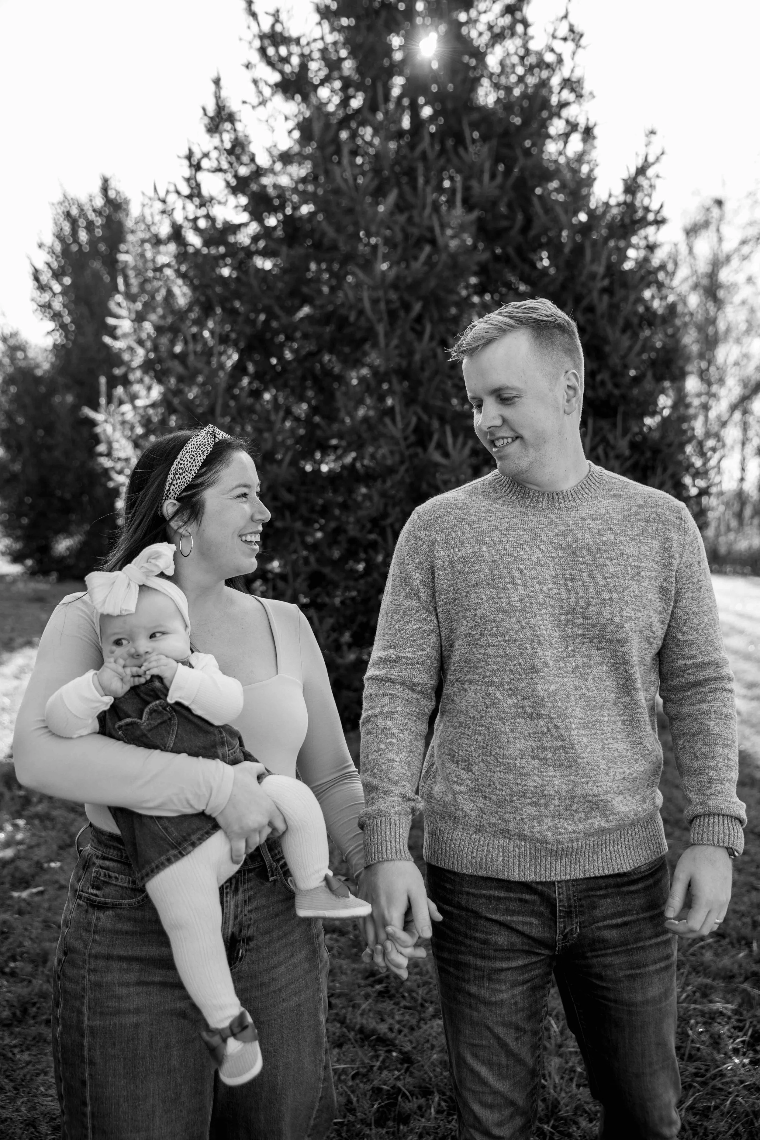 mother and father holding hands walk laughing with baby