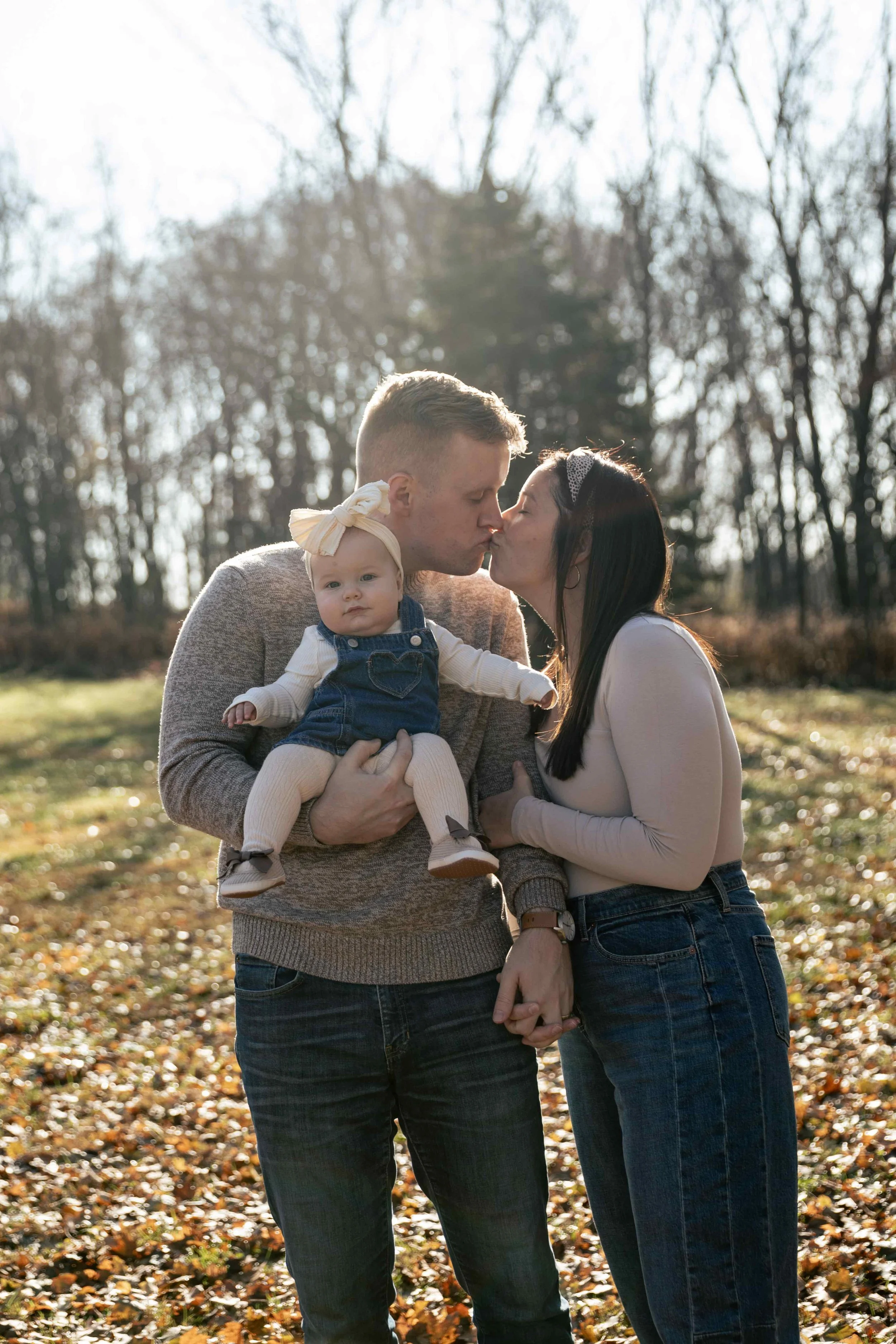 mother and father kiss while baby smiles
