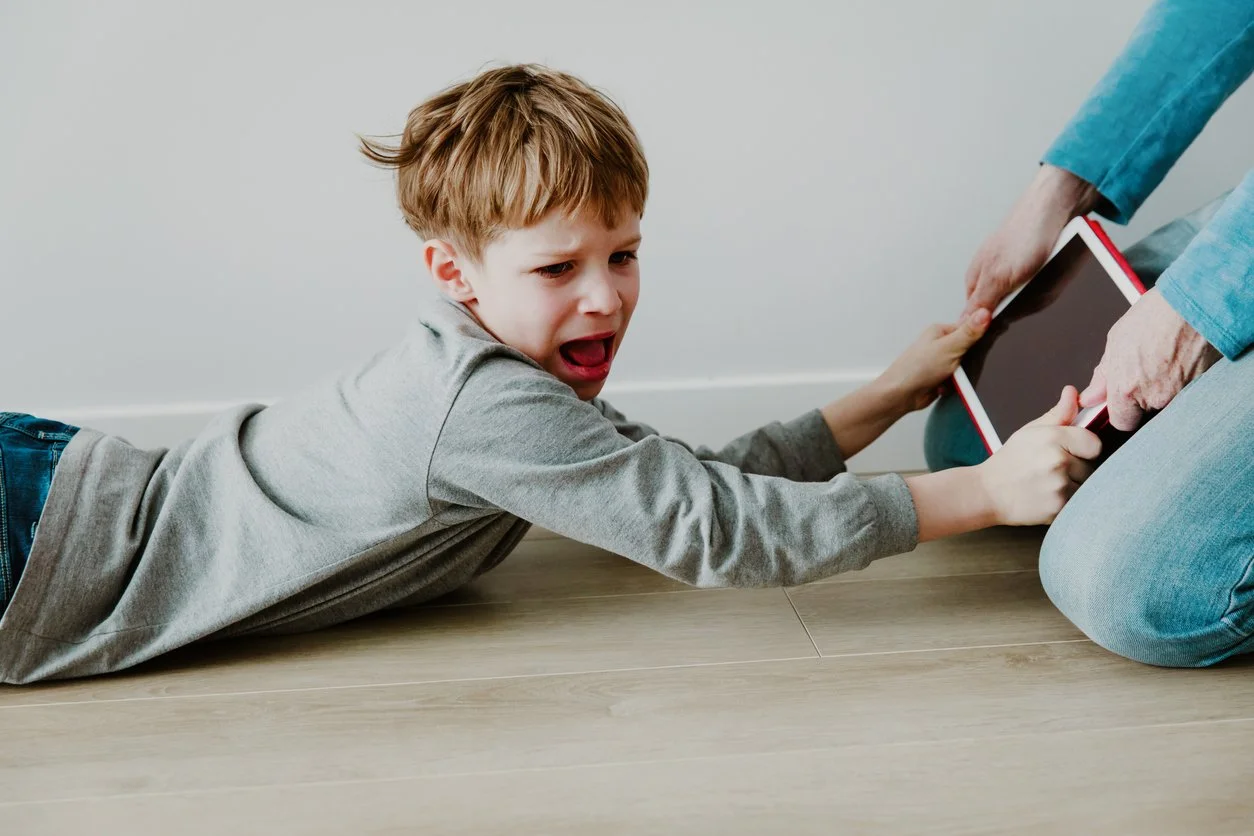 A mom trying to pull an ipad out of her child's hands
