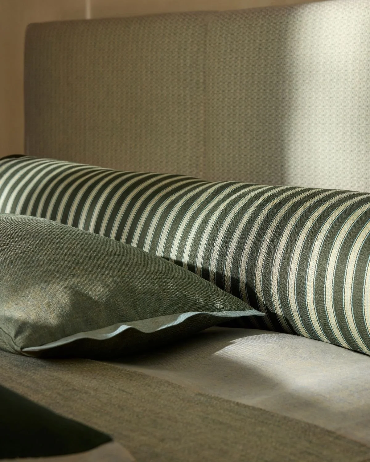Ian Mankin Earthlight Linens Collection featuring layered green linen cushions and a striped bolster cushion.