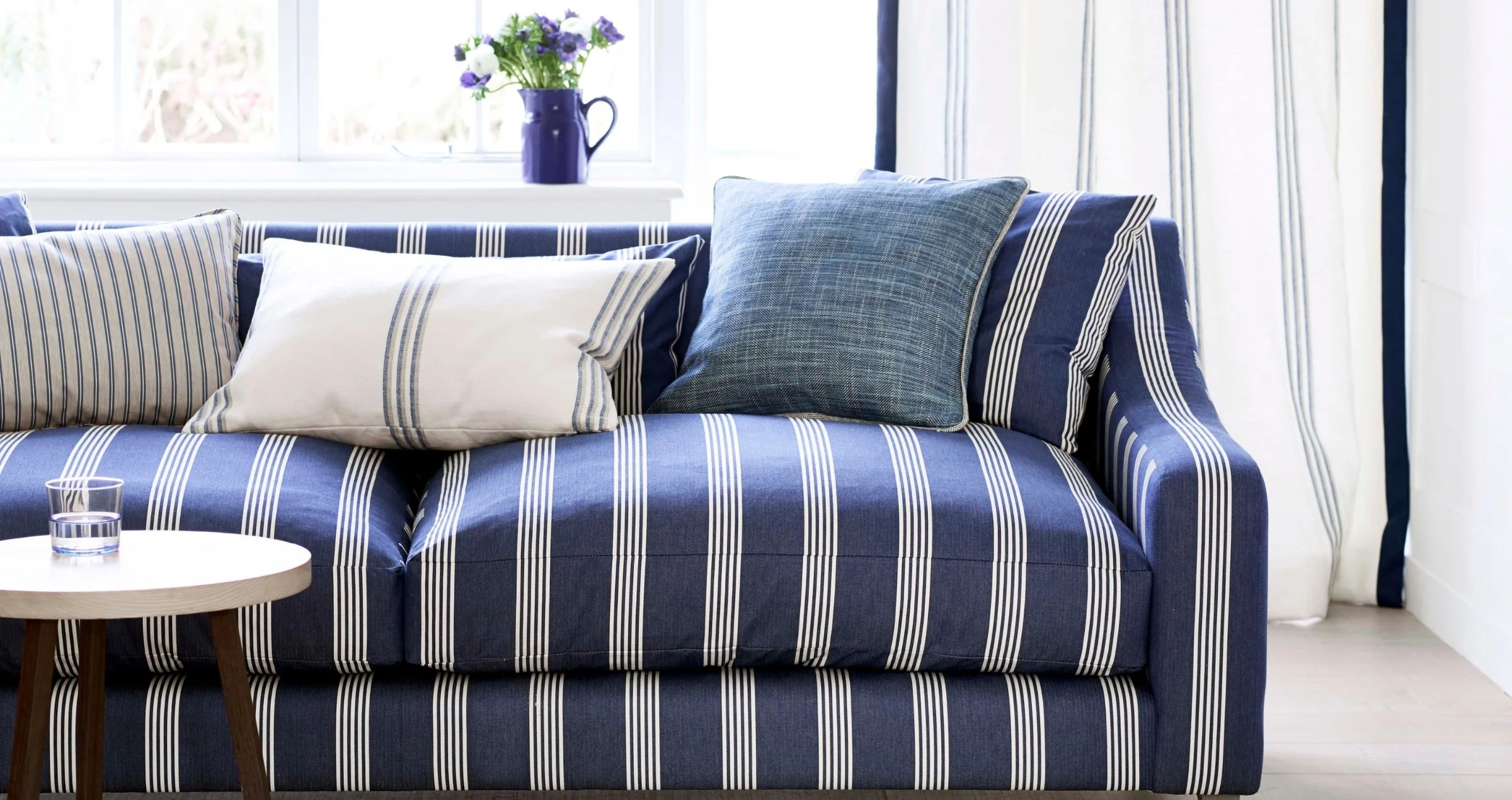 Ian Mankin Oxford Navy striped fabric upholstered sofa in a blue and white living room with coordinating cushions and curtains.
