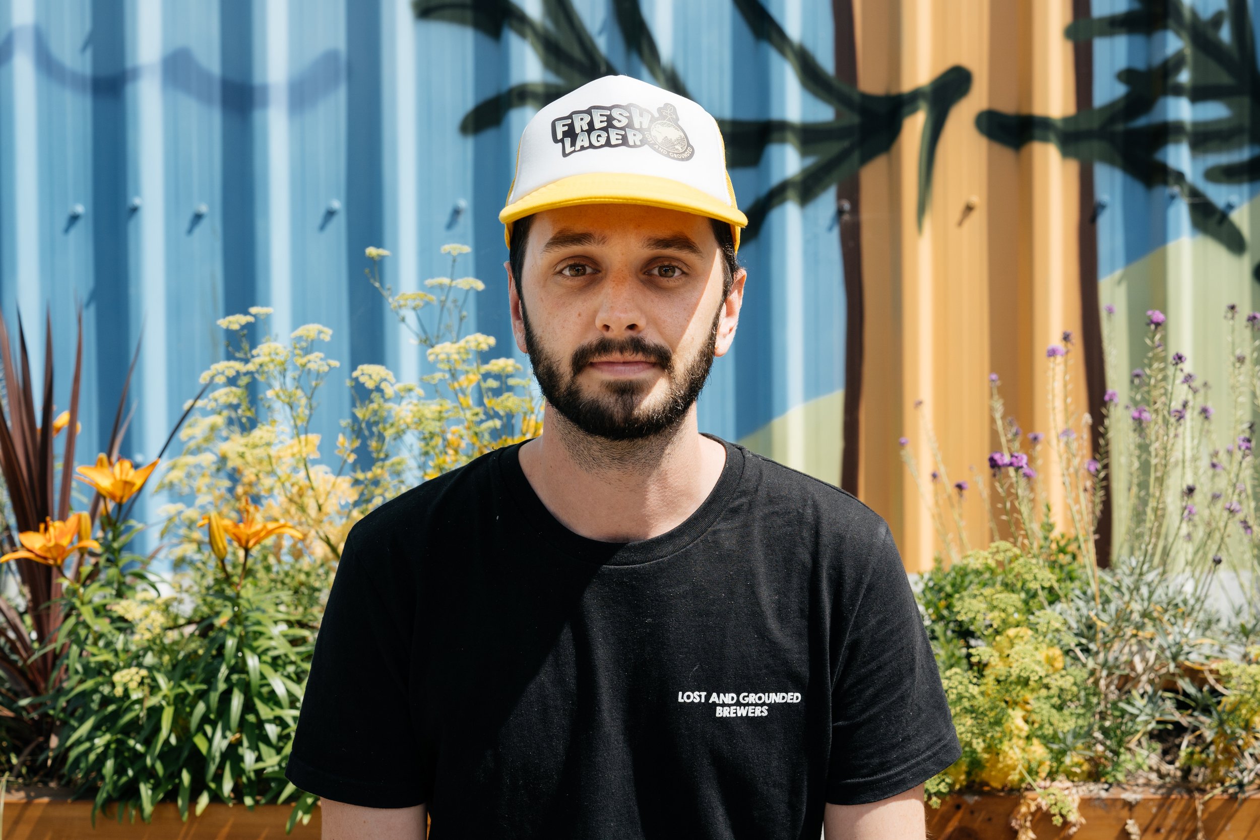 Man outside looking at the camera with yellow trucker hat with fresh lager and Lost and grounded logo on front.