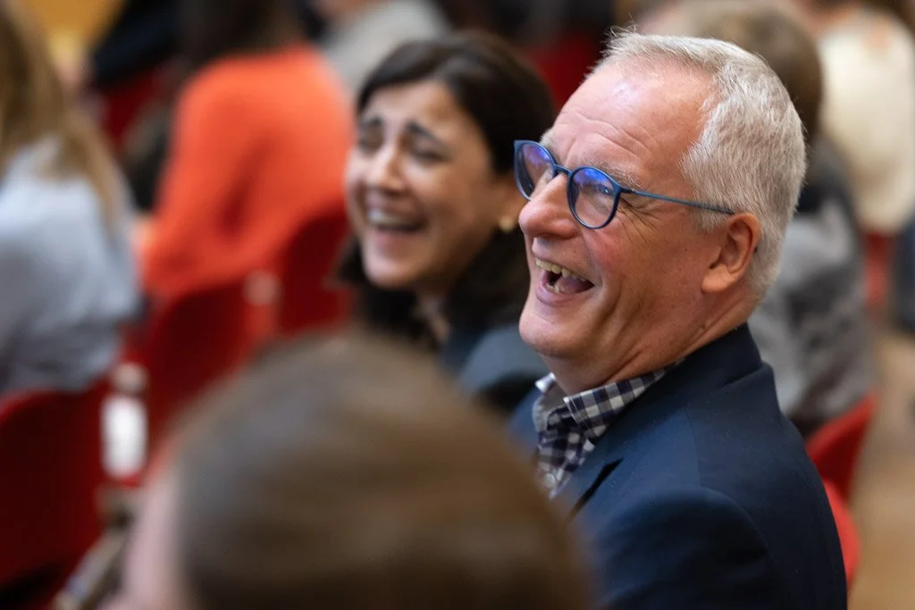 Spontant og glædesfyldt øjebliksbillede af grinende publikum under foredrag.