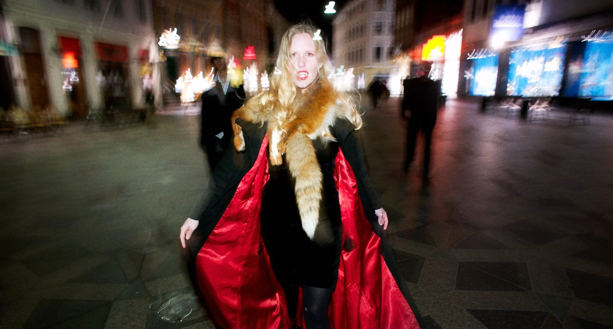 Rollespilsfoto ved Steen Brogaard. Kvinde med åbenstående jakke, nattescene i by-mljø. vampyrtænder og rødt for. 
