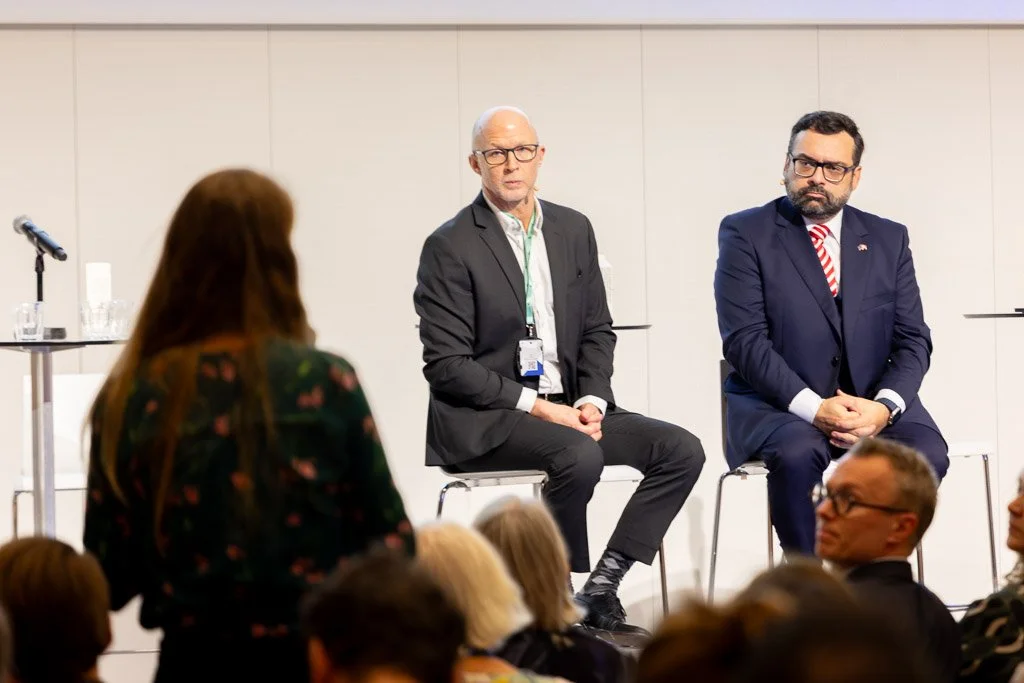 Dynamisk konferencefoto af panel på scene der lytter til spørgsmål fra publikum.