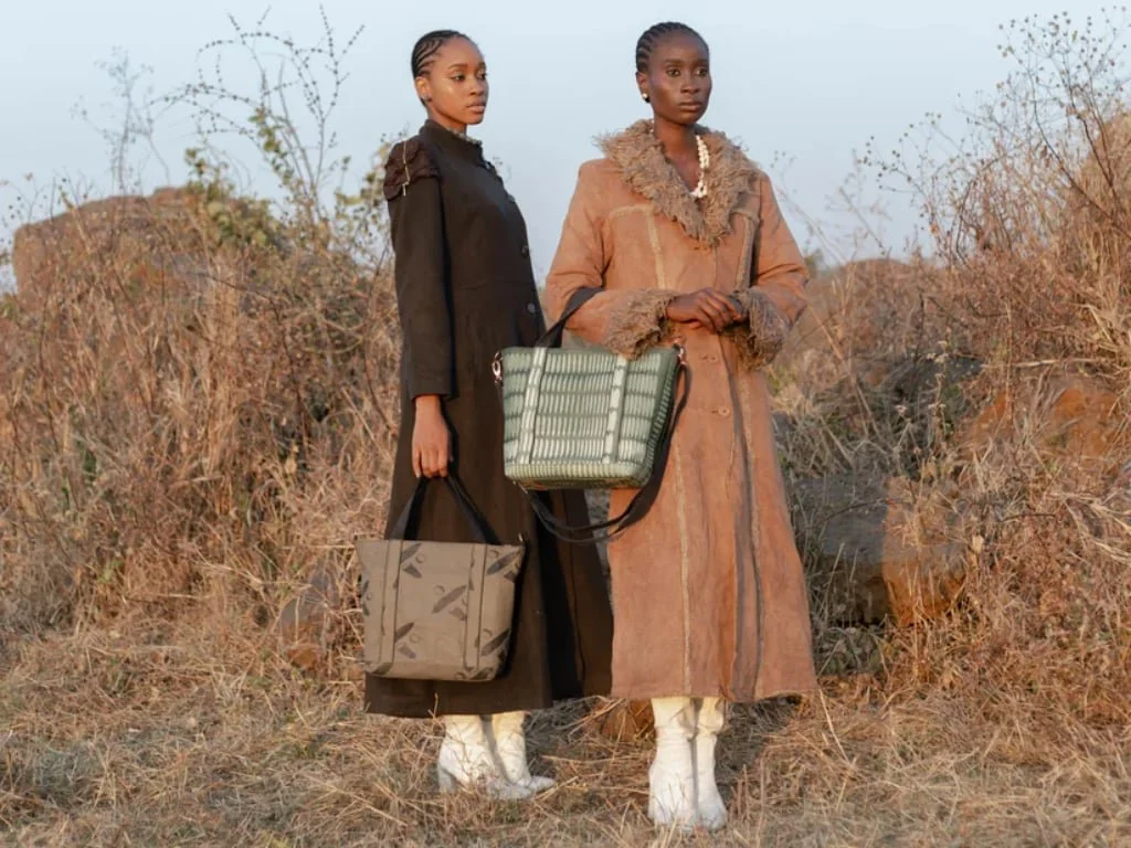 Two women holding Udiri bags wearing long jackets and white boots