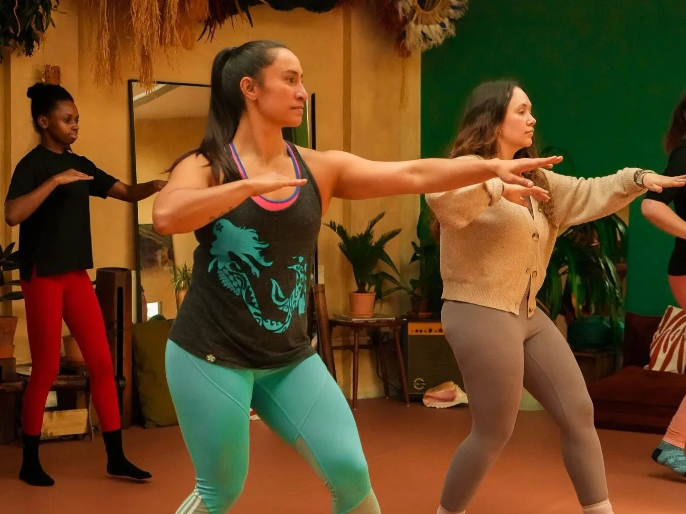 Women practicing hula dancing in a room with plants and warm lighting, focusing on balance and mindfulness.