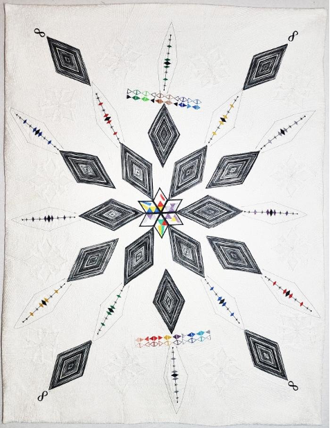 A photograph of a textile work. Monochrome diamonds pan out in rags from a 12 pointed star which contains brightly colored small diamonds.