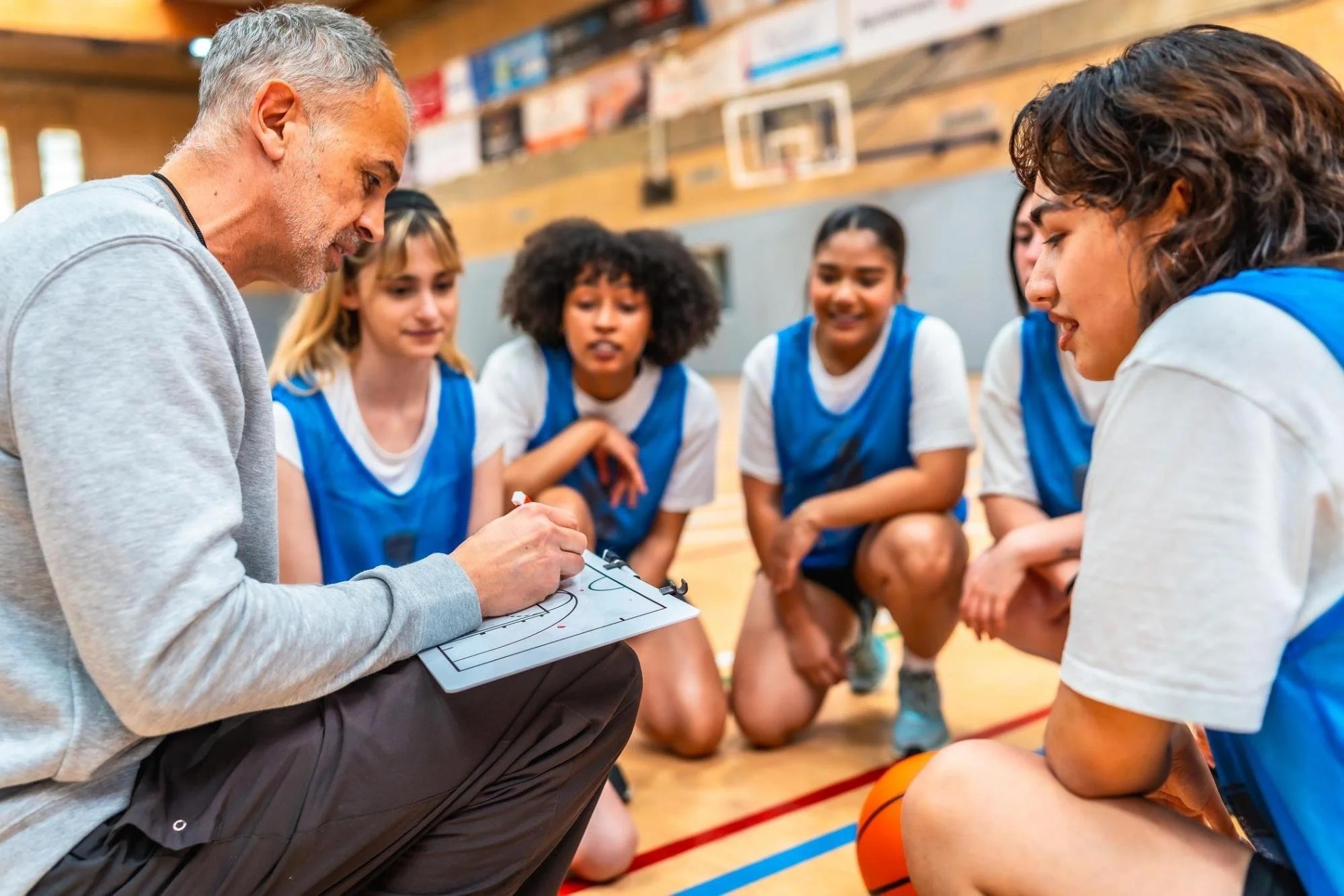 Basketball coach teaching female players during timeout in gym.