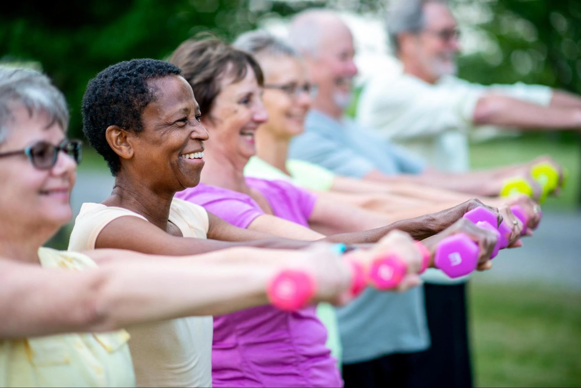 Group of diverse seniors doing outdoor exercise with dumbbells, smiling and stretching their arms