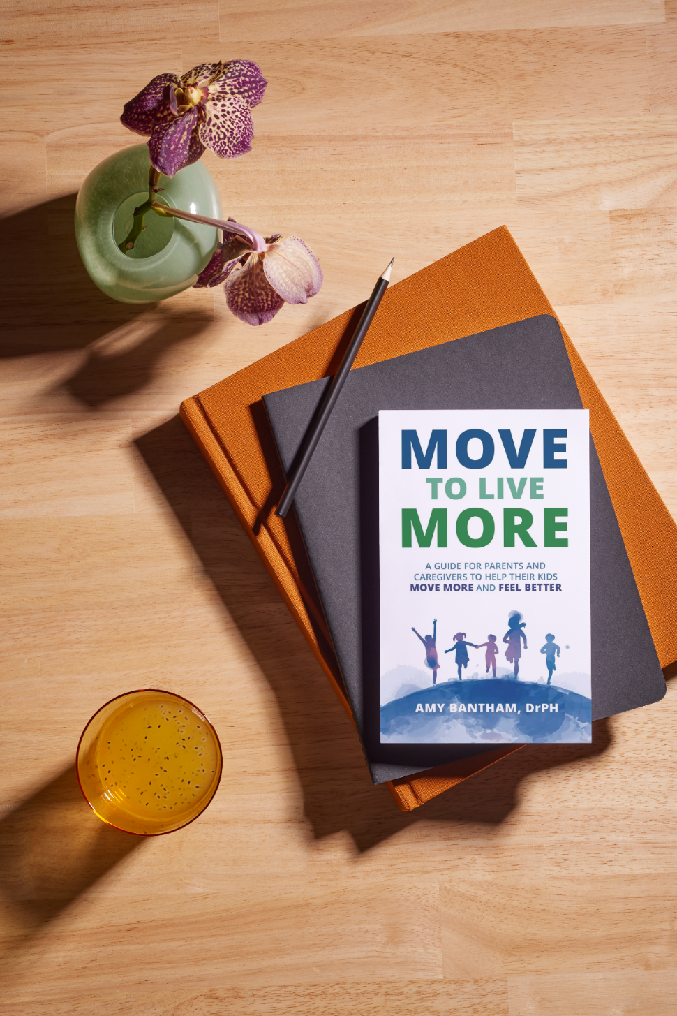 A table with a vase of purple orchids, a glass of orange juice, and a stack of books with a booklet titled "Move to Live More" on top.