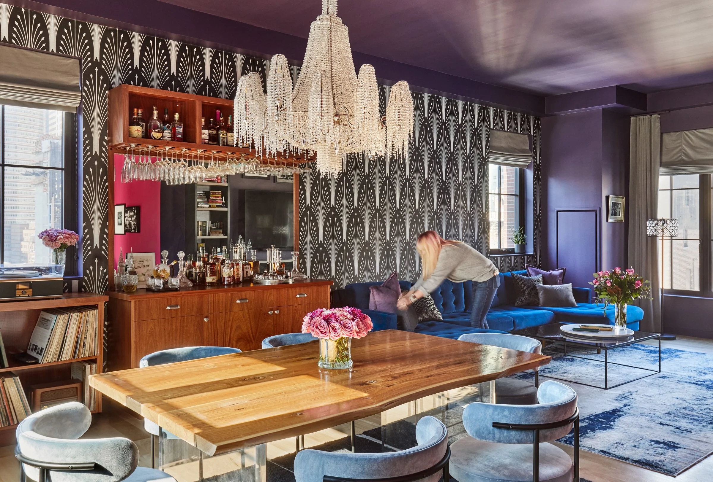 color drenched living room's wall and ceiling in grape with art deco inspired wallpaper off-set the custom bar and crystal chandelier