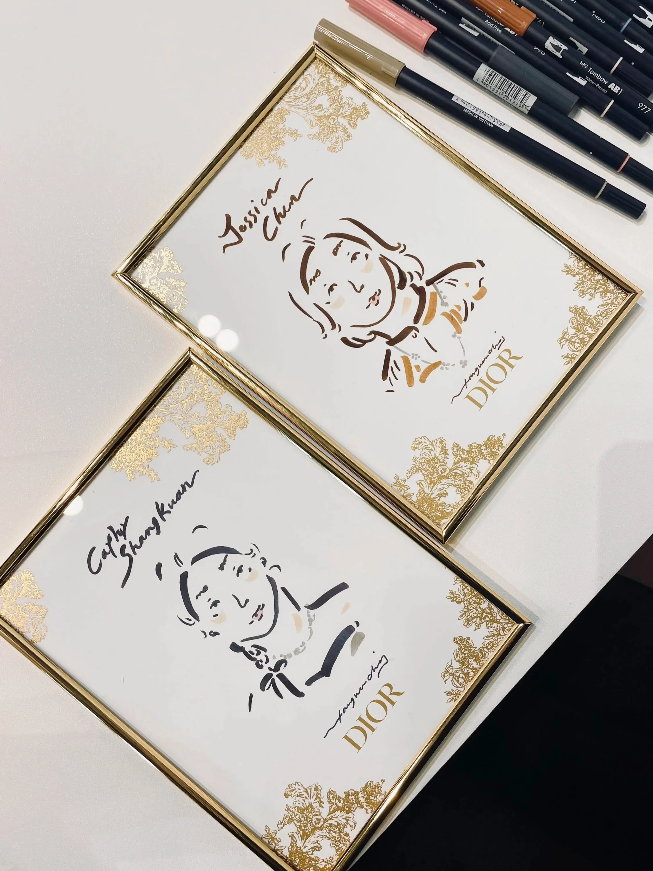 Two ornate gold-framed prints displayed face-up, each featuring a minimalist line drawing of a woman's face in a classical illustration style by Tang Wen Ching
