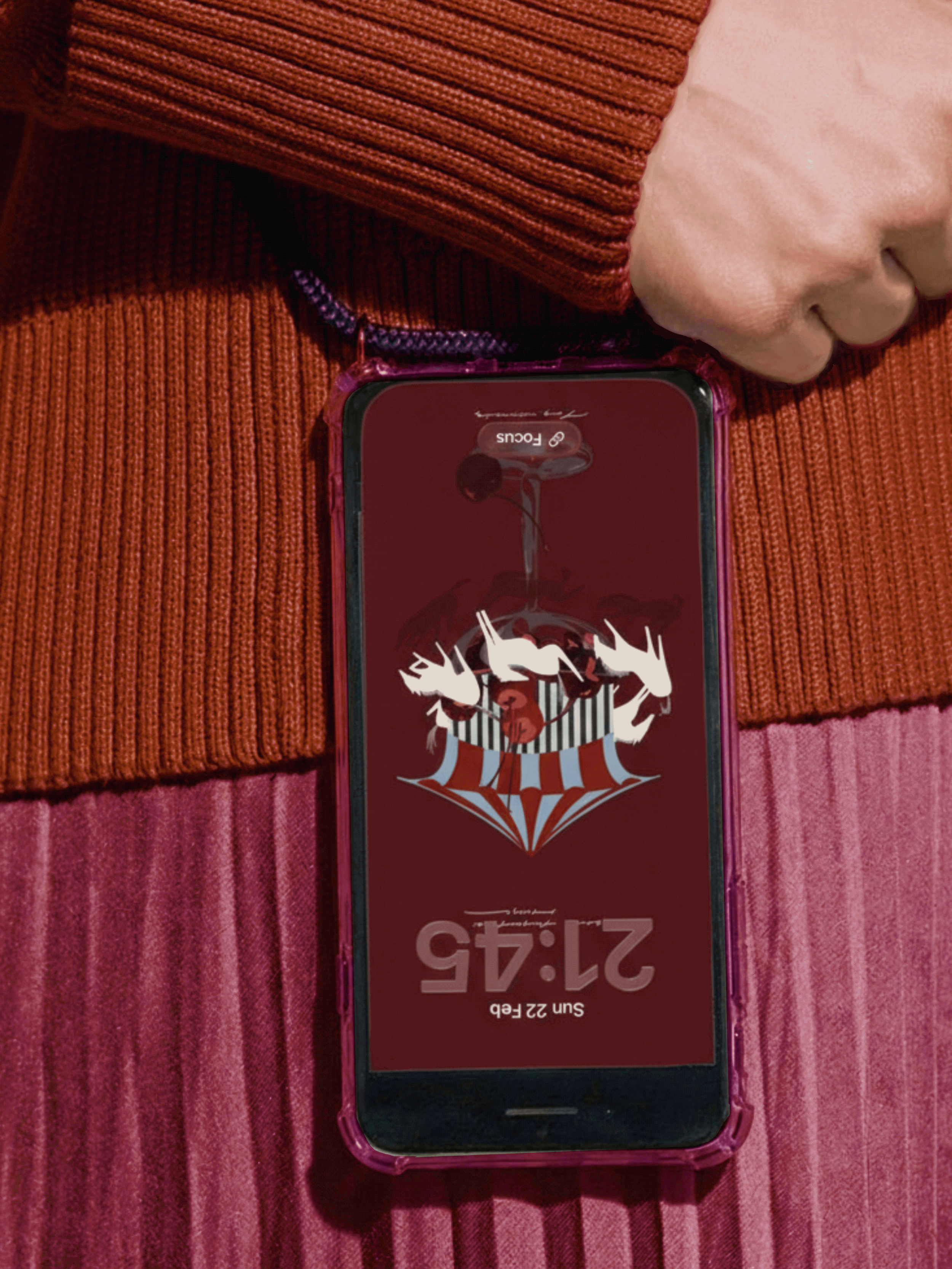 A smartphone with a pink case displaying a barcode, placed on a multicolored striped fabric surface.