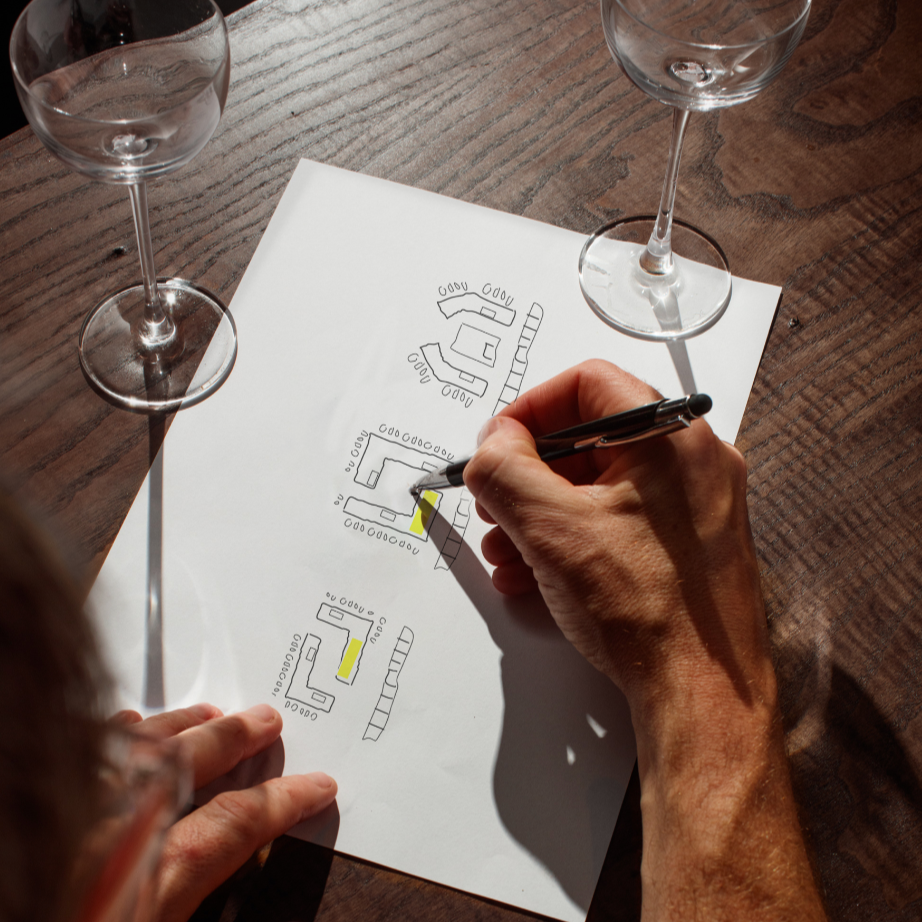 Bar designer sketching different bar layouts on white paper on a wooden table, with two empty cocktail glasses nearby.