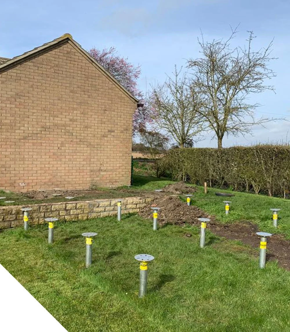 image shows groundscrews placed in a garden next to a brick-built building ready for a lodge
