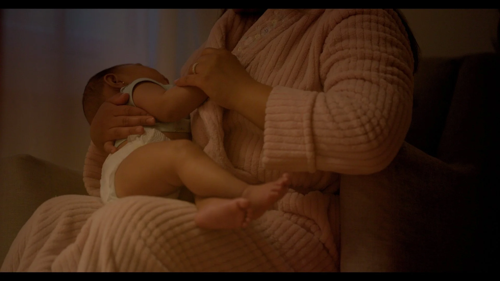 A baby breastfeeding from a woman wearing a pink, textured sweater.