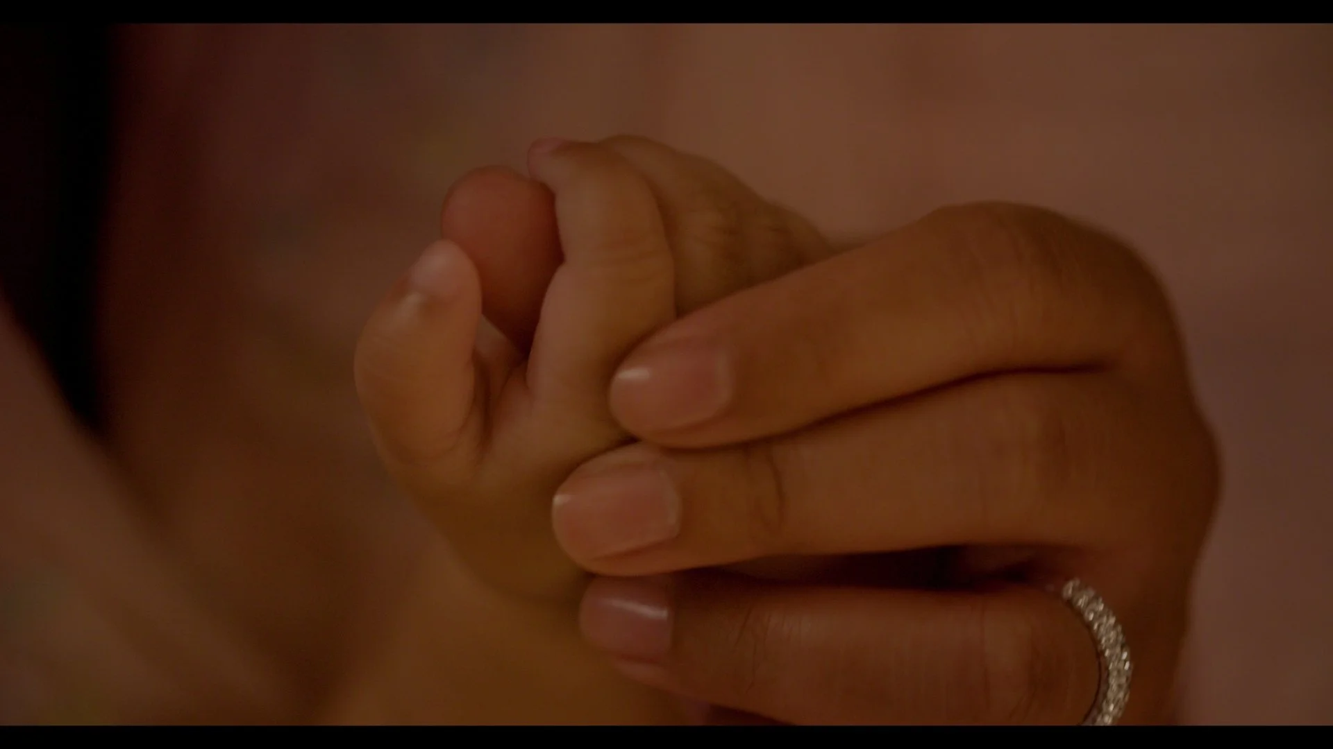 Close-up of an adult hand holding a baby's hand.