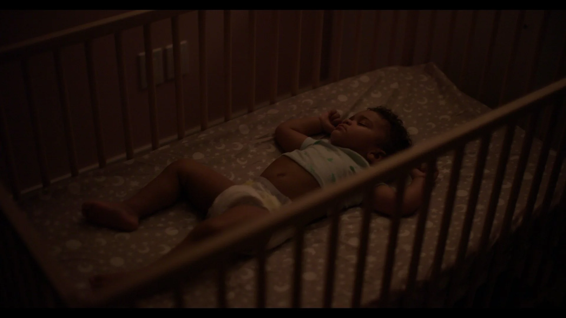 A young child sleeping in a crib at night.