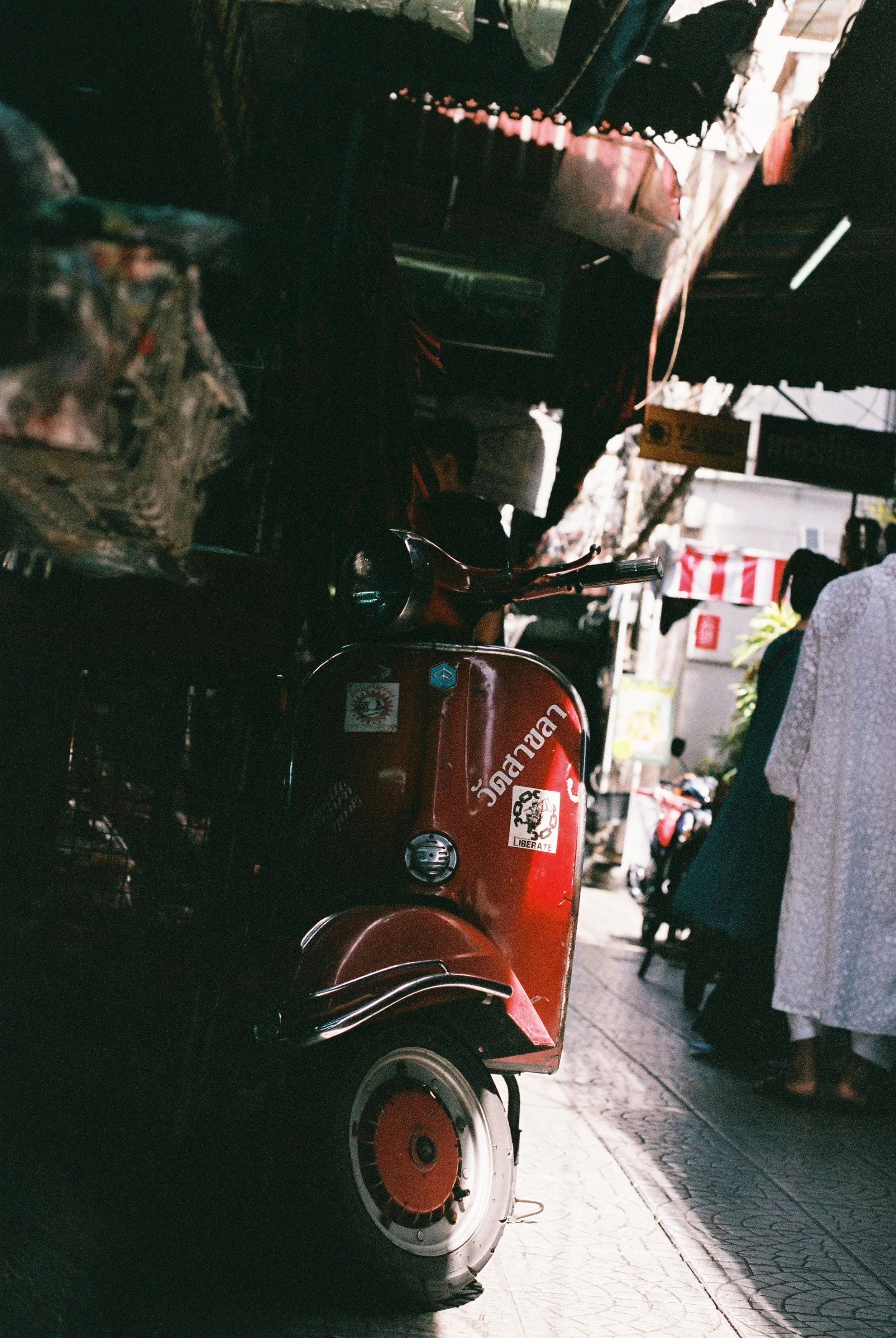 A red scooter parked on a busy street, with people walking nearby and market stalls in the background.