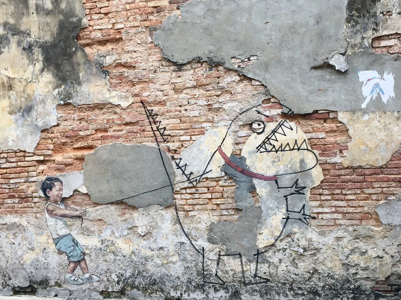 Street art on a weathered brick wall depicting a cartoonish dog wearing a red collar and a child pulling on the dog's tail, with some torn posters on the wall.