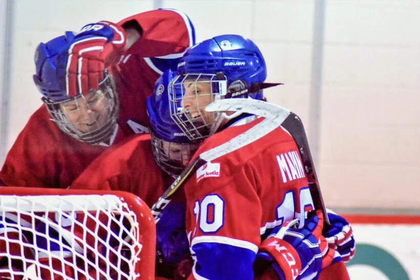 Ice hockey players in red and blue jerseys celebrating near the goal post.
