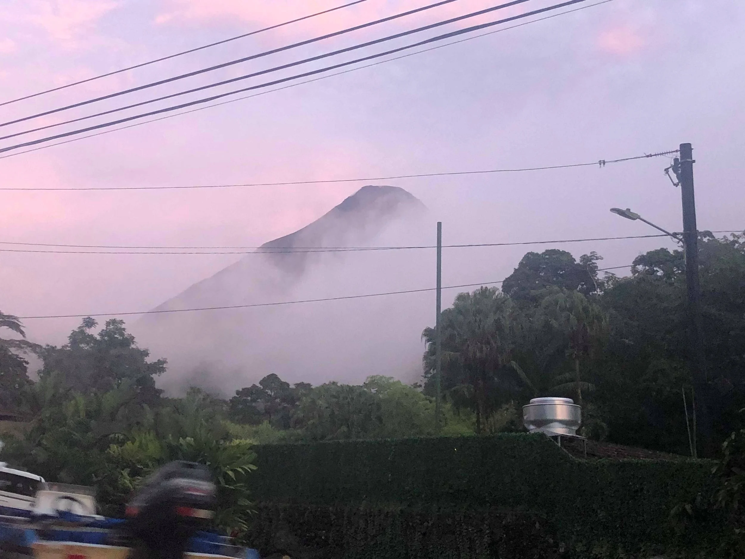 Mountain with clouds or fog at sunrise or sunset, with power lines and trees in the foreground