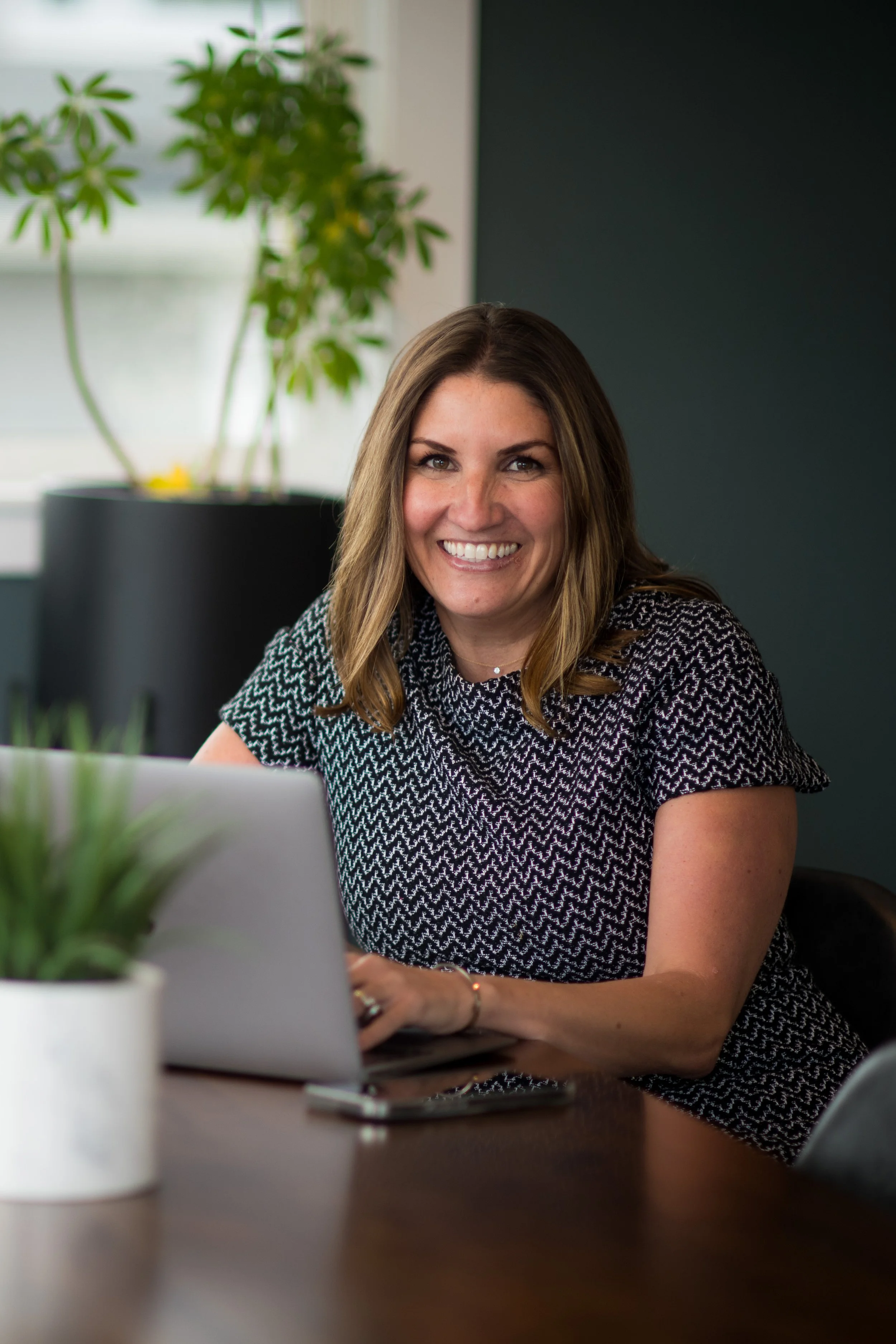a woman, paige schulte, sits at a desk with her laptop smiling