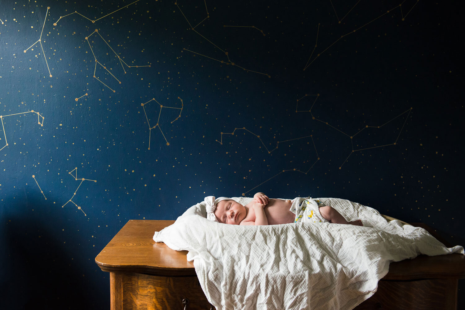 little newborn resting in a bed with a constellation painted on the wall behind