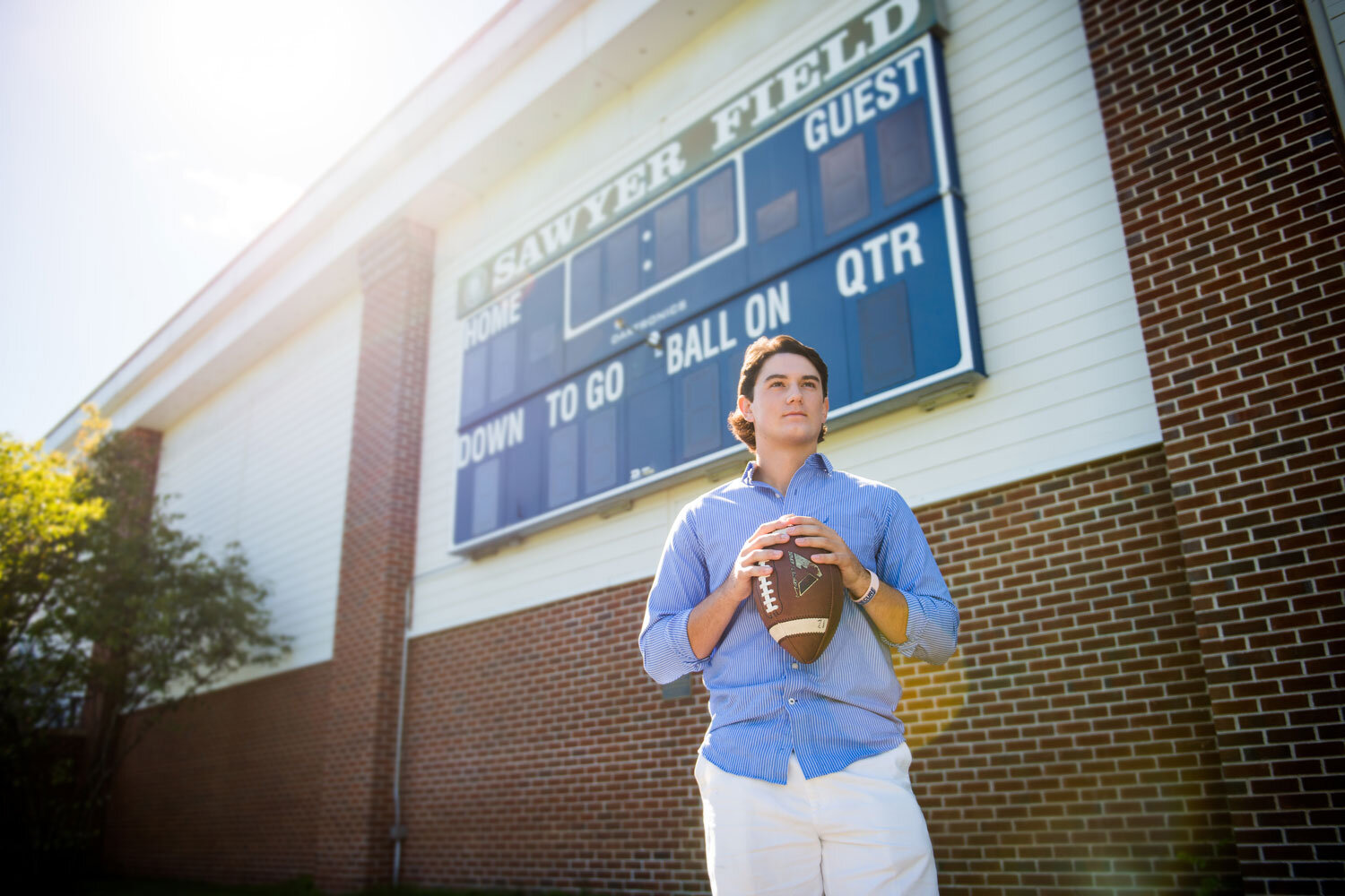 high school foot baller wearing a blue shirt standing in a field holding a football