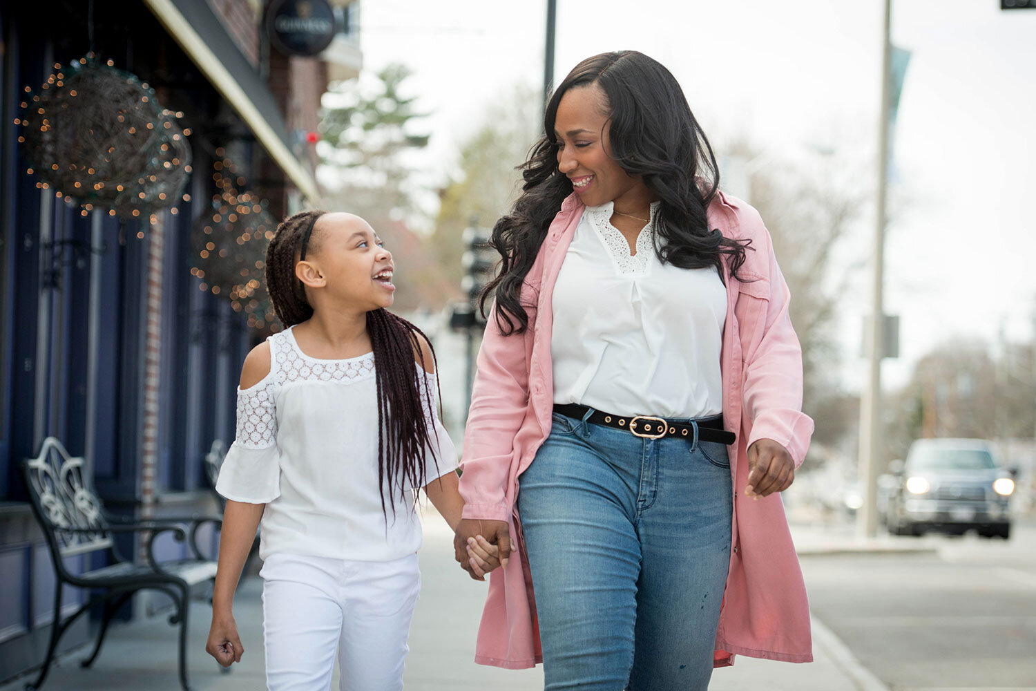 Black mom and daughter walking down a city street looking at one another and smiling