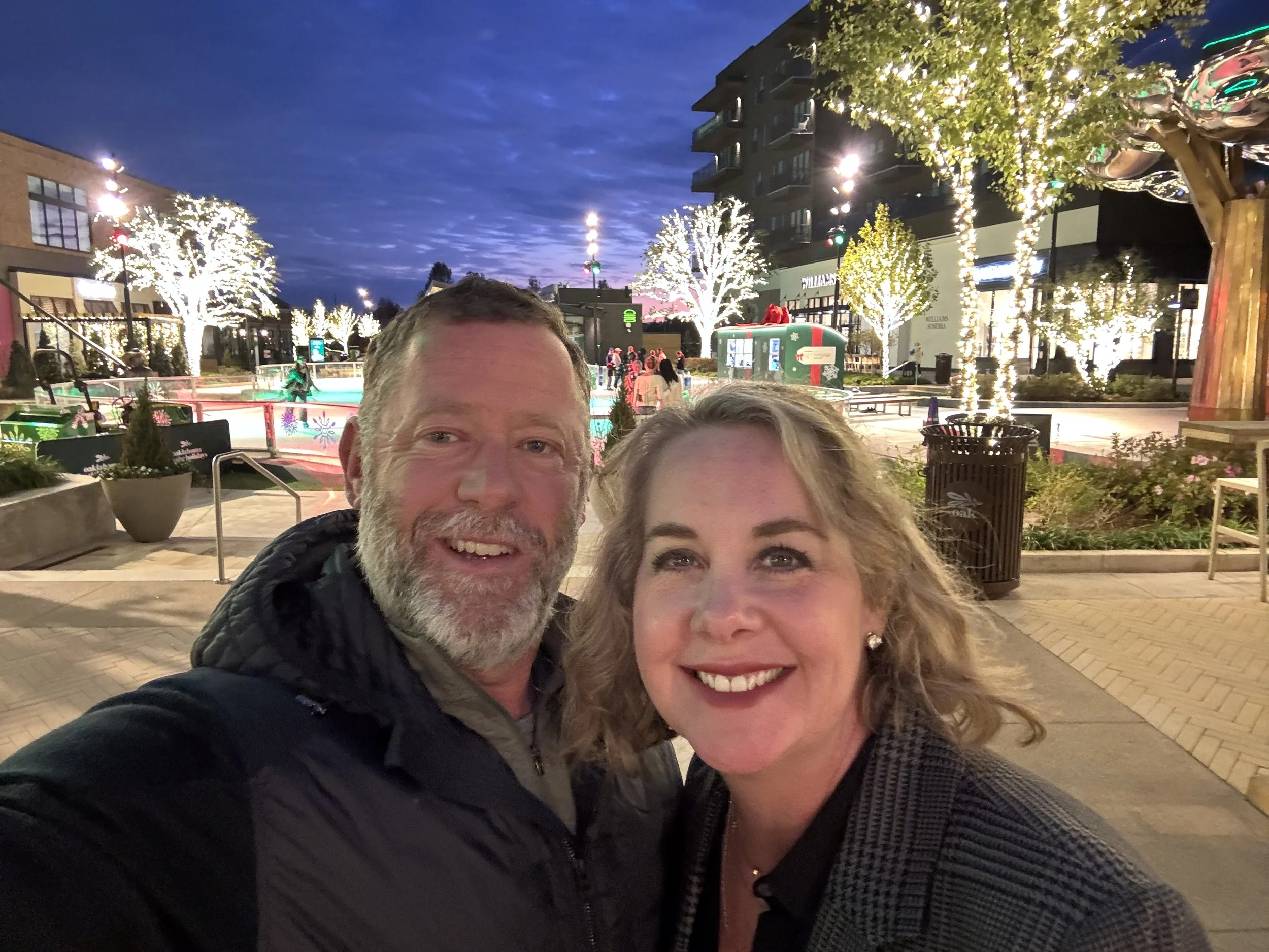 A woman wearing glasses and a yellow beanie is smiling while making a coffee at a cafe counter.