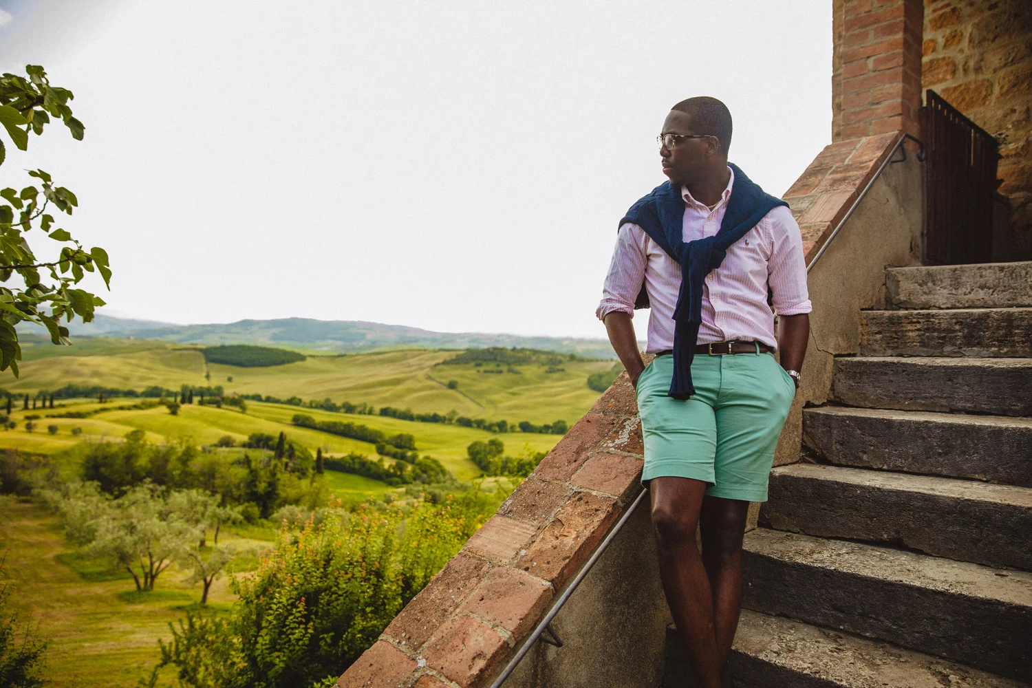 Maurice Jackson wearing a pink striped Oxford shirt and pastel chino shorts overlooking the Tuscan countryside