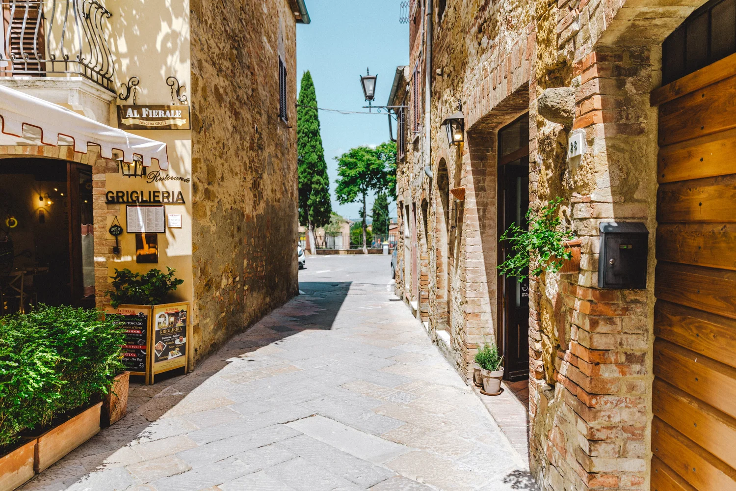 Restaurant storefronts and stone buildings along a narrow street in Pienza
