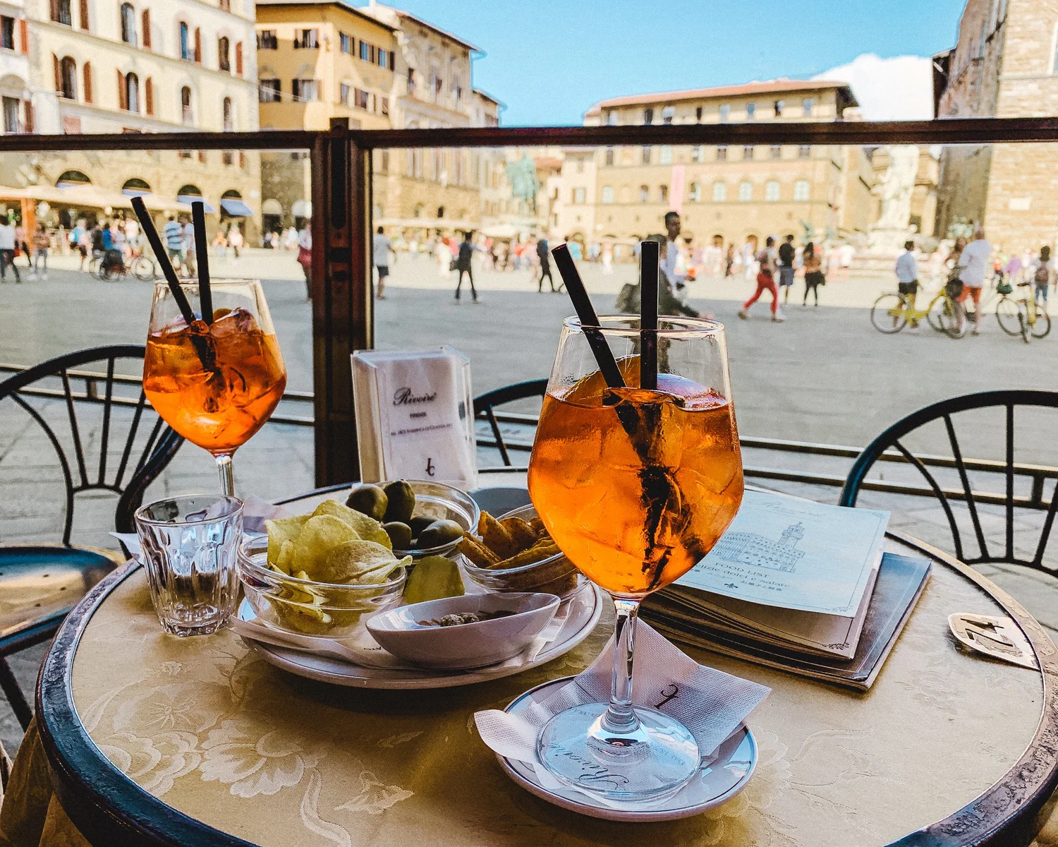 Two Aperol Spritz cocktails at a café overlooking an Italian piazza