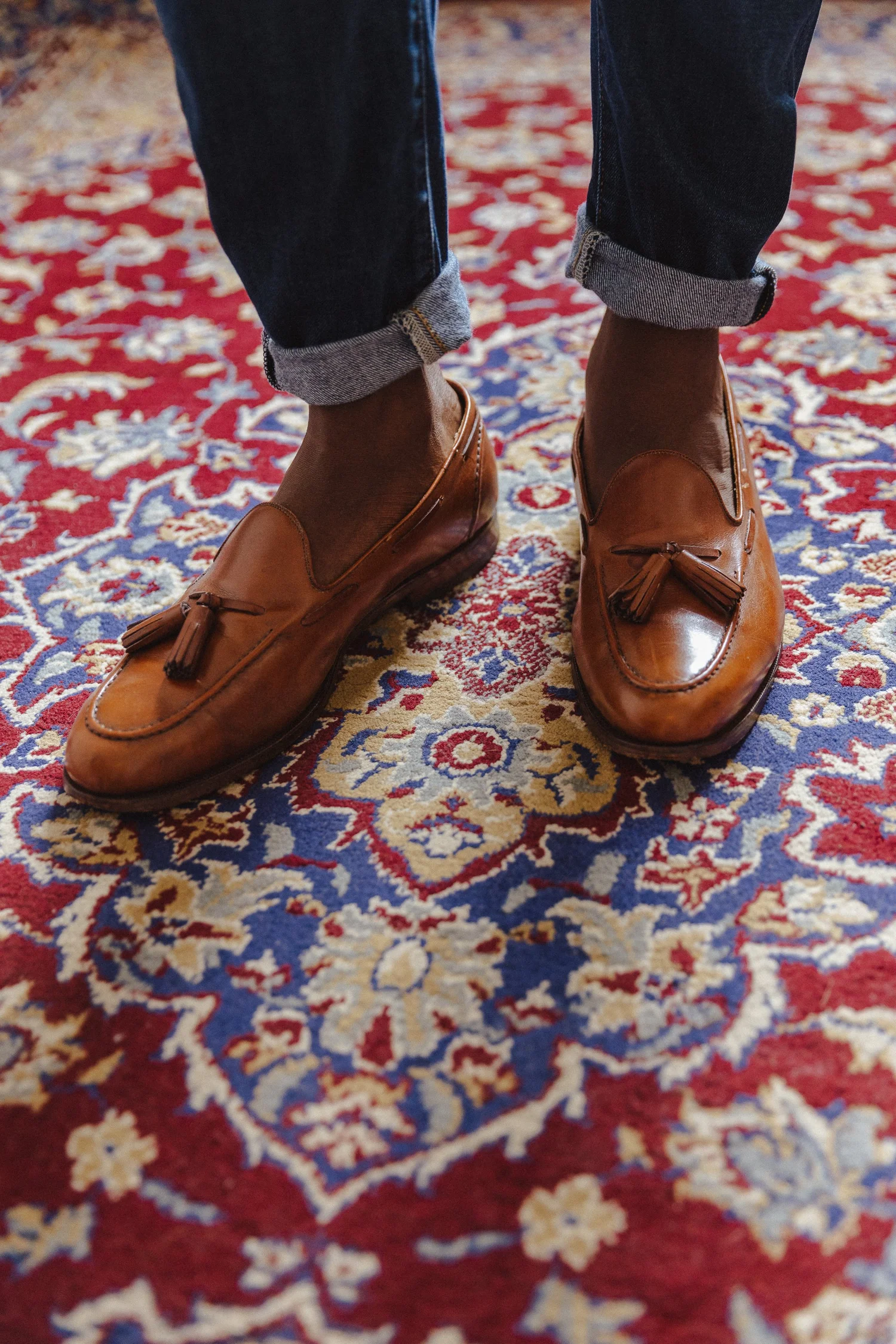 Cuffed jeans and brown tassel loafers on a patterned rug