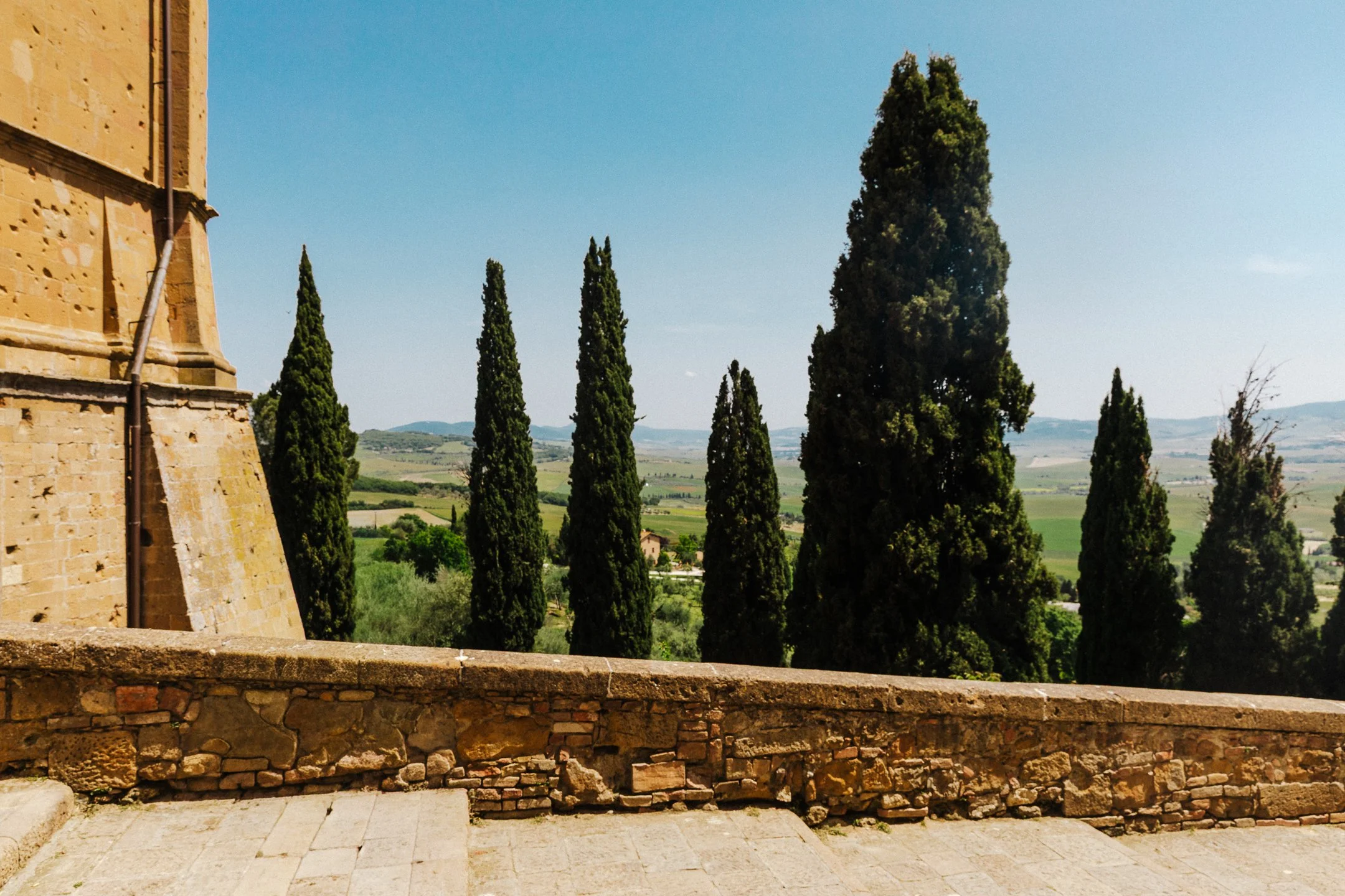 Cypress trees beside a stone wall overlooking the Tuscan countryside in Pienza