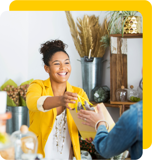 Woman in yellow jacket accelerates business by handing a package to a customer with a big smile.