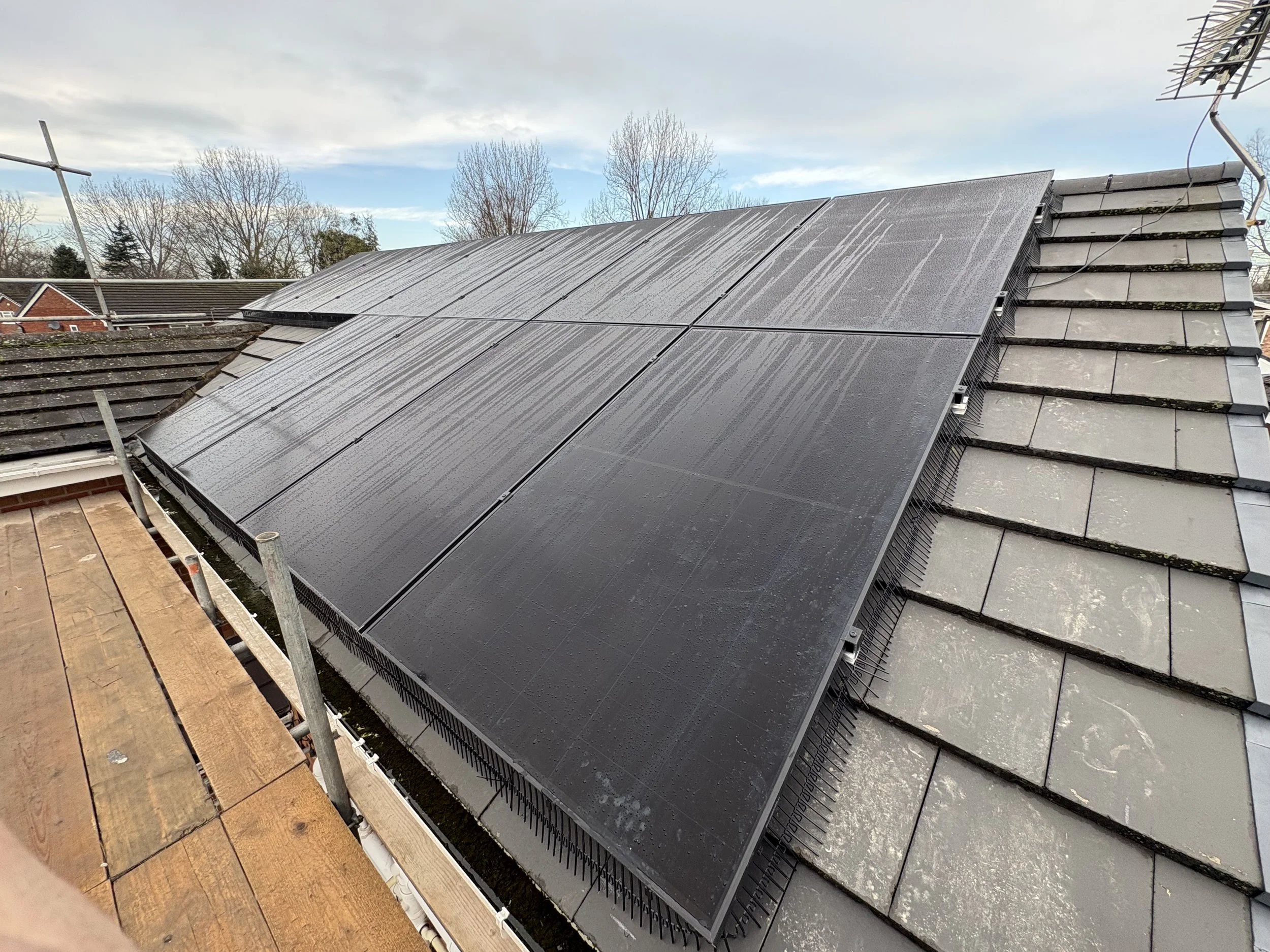 Solar panels installed on a sloped roof, with a background of trees and a cloudy sky.