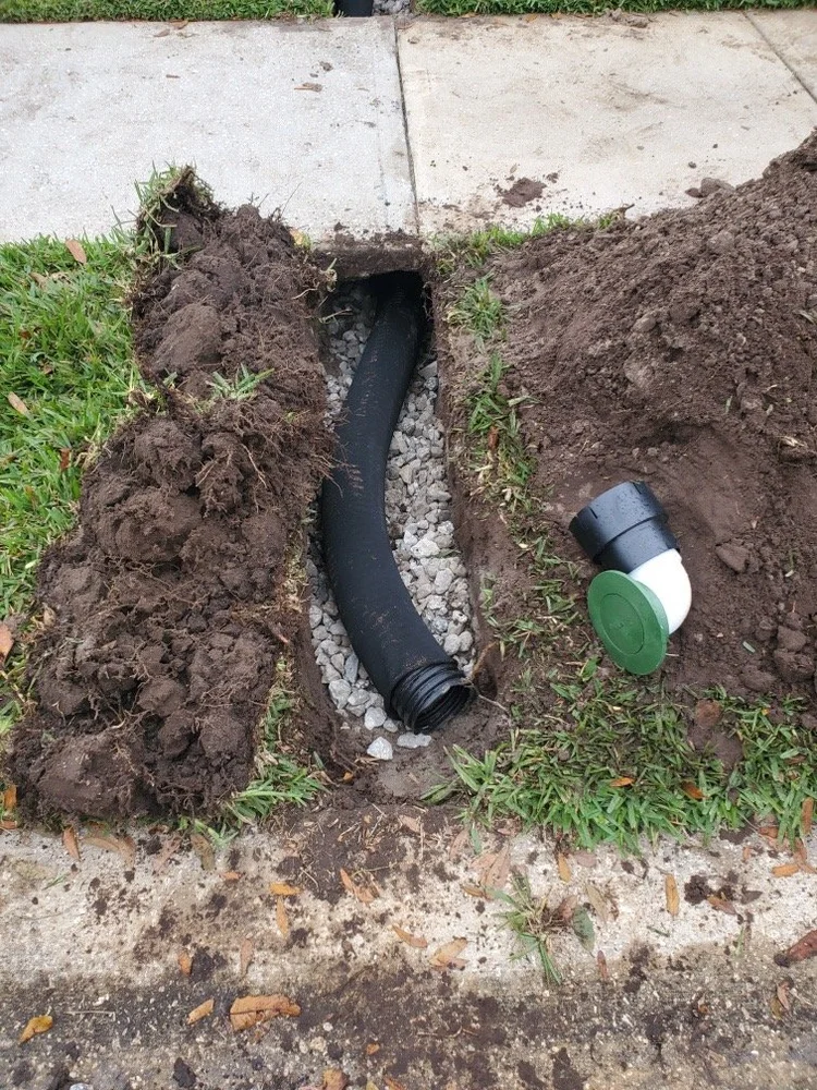 Drain pipe in gravel with a green pop-up emitter at the outlet