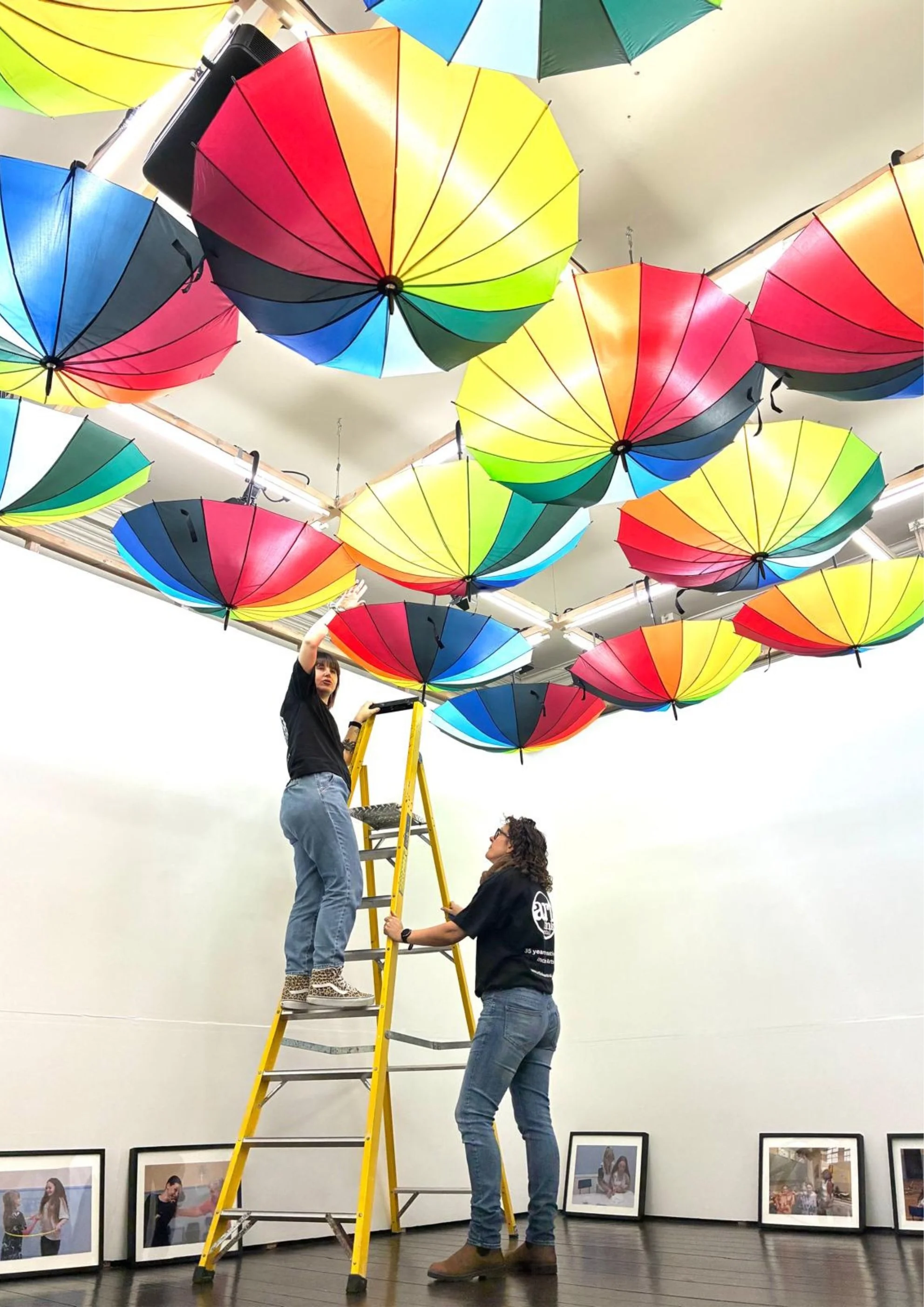 Photo by Julie Howden, Artlink Central team installing rainbow umbrellas in the Tolbooth Gallery using a yellow ladder for a Stirling 4 Families exhibition